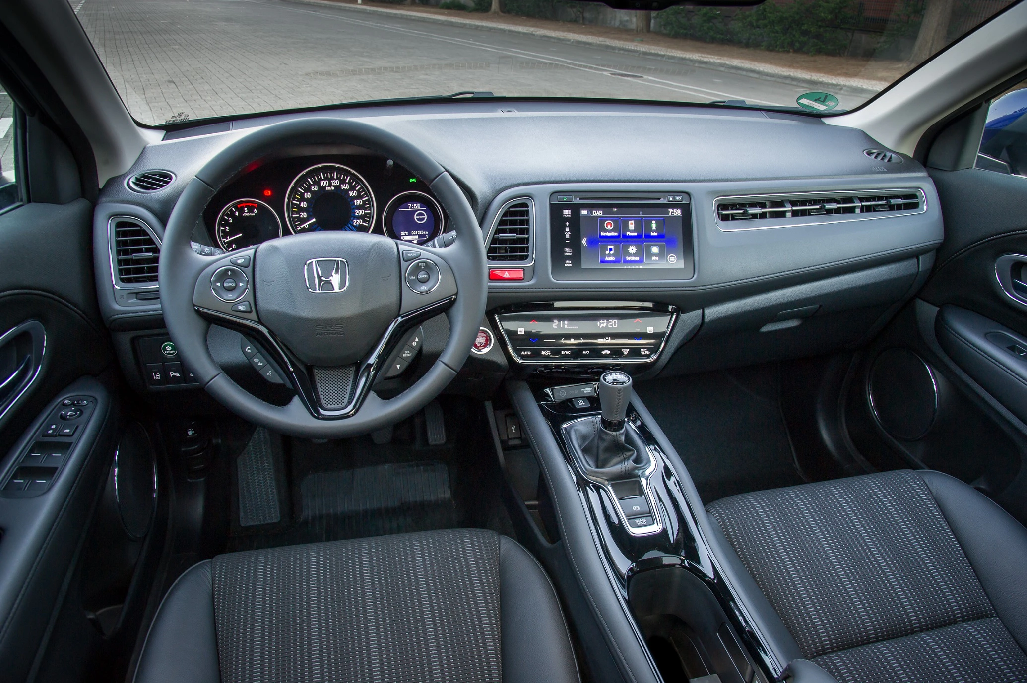 Innenraum eines modernen Autos mit Honda-Logo am Lenkrad, digitalem Armaturenbrett, Touchscreen und Schalthebel, schwarz-graue Sitze.