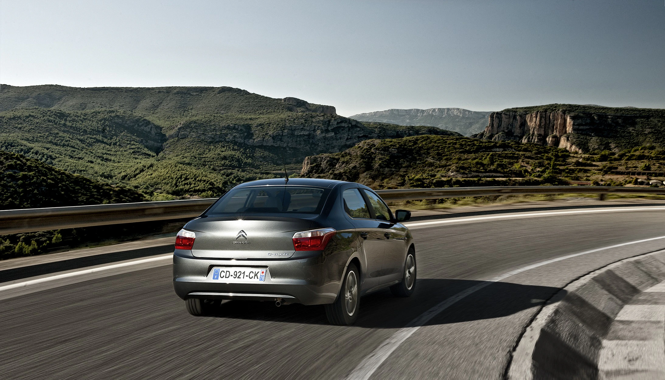 Ein grauer Citroën fährt auf einer kurvigen Straße durch eine bergige Landschaft unter klarem Himmel.