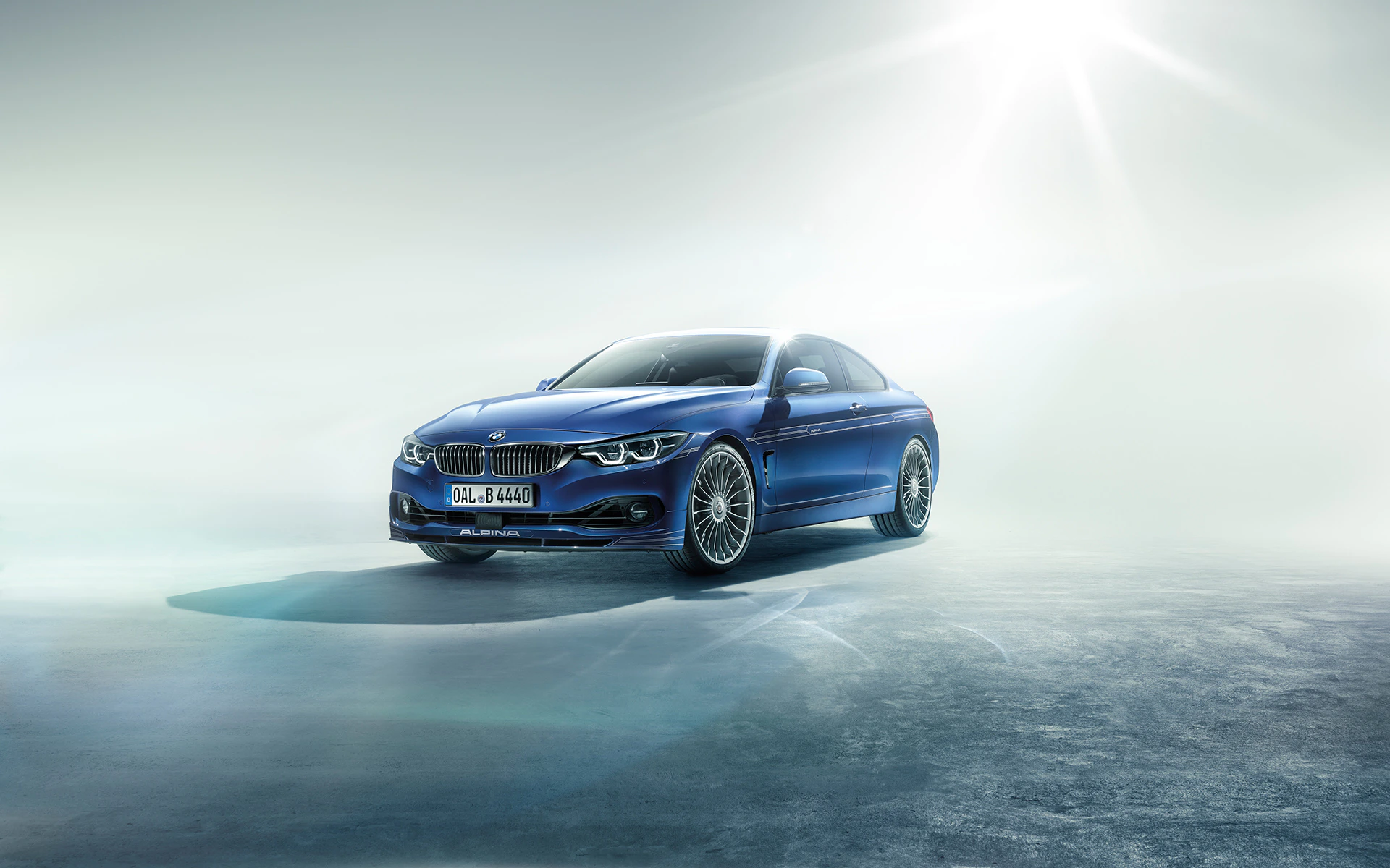 Blauer Sportwagen auf spiegelndem Boden, bei diffusem Licht. Schriftzug "Alpina" erkennbar. Hintergrund ist neblig mit Sonnenlicht von oben.