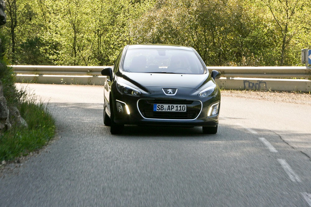 Schwarzer Peugeot 308 fährt auf einer kurvigen Landstraße, umgeben von Bäumen.