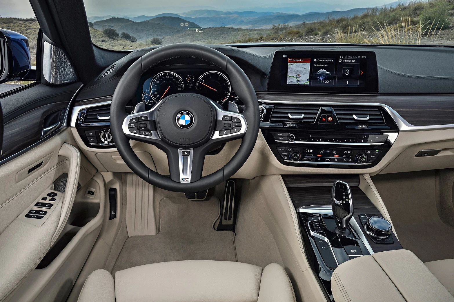 Innenraum eines BMW mit hellem Leder, Multifunktionslenkrad und digitalem Display. Blick auf das Lenkrad und Armaturenbrett.