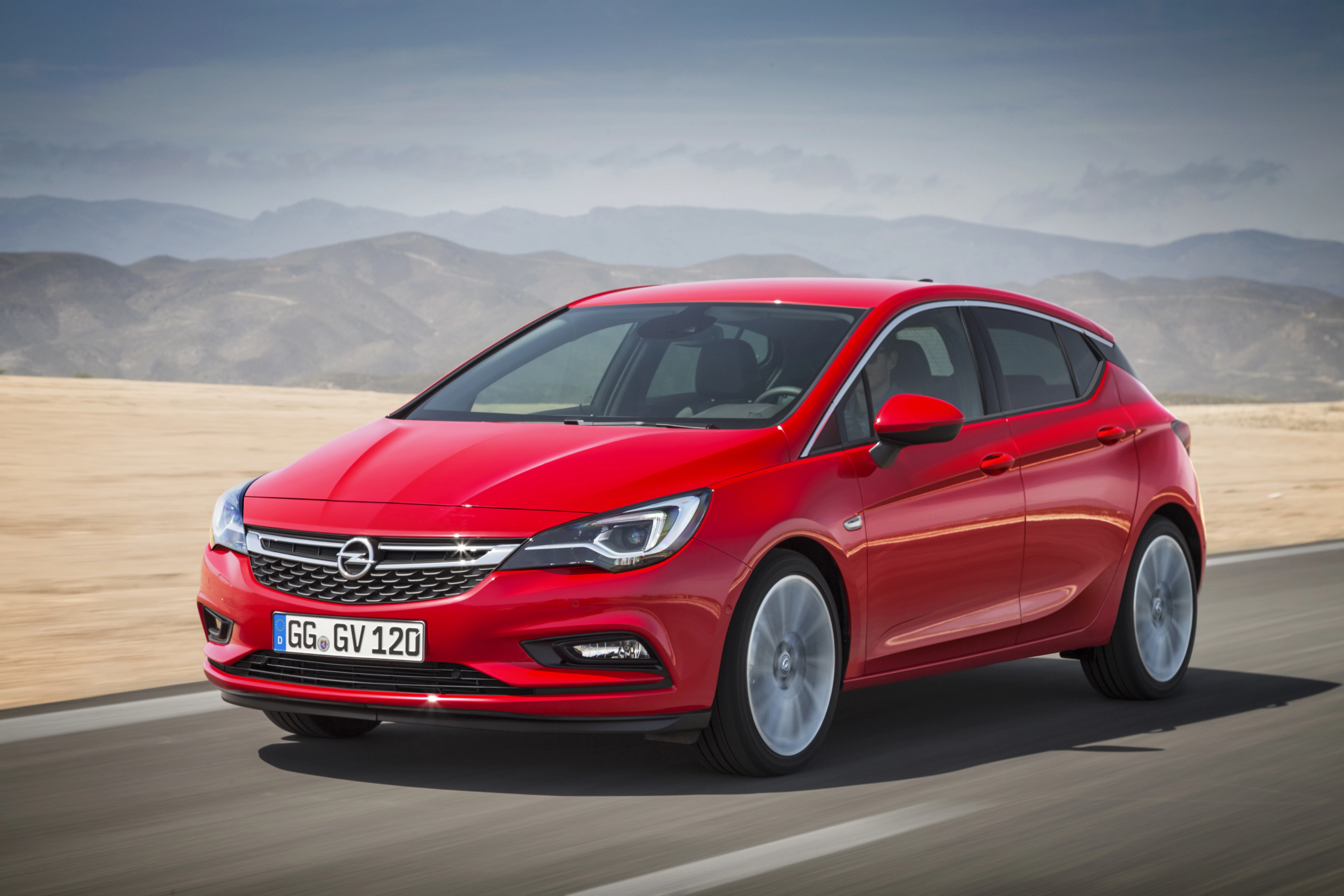 Roter Opel Astra fährt auf einer Straße in einer Wüstenlandschaft, umgeben von Bergen.