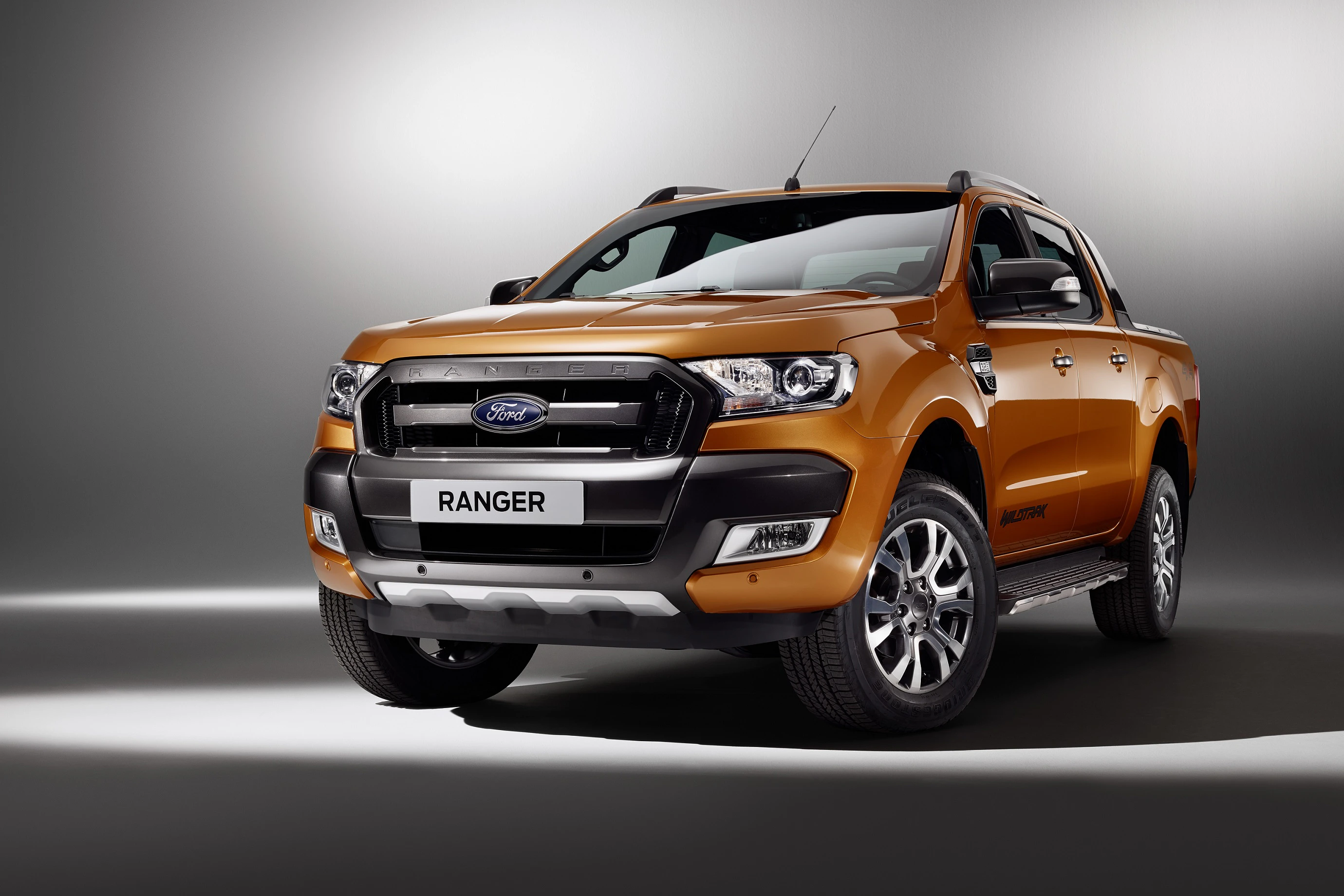 Orangefarbener Ford Ranger Pickup in einem Studio vor grauem Hintergrund, mit beleuchteten Details und glänzendem Lack.