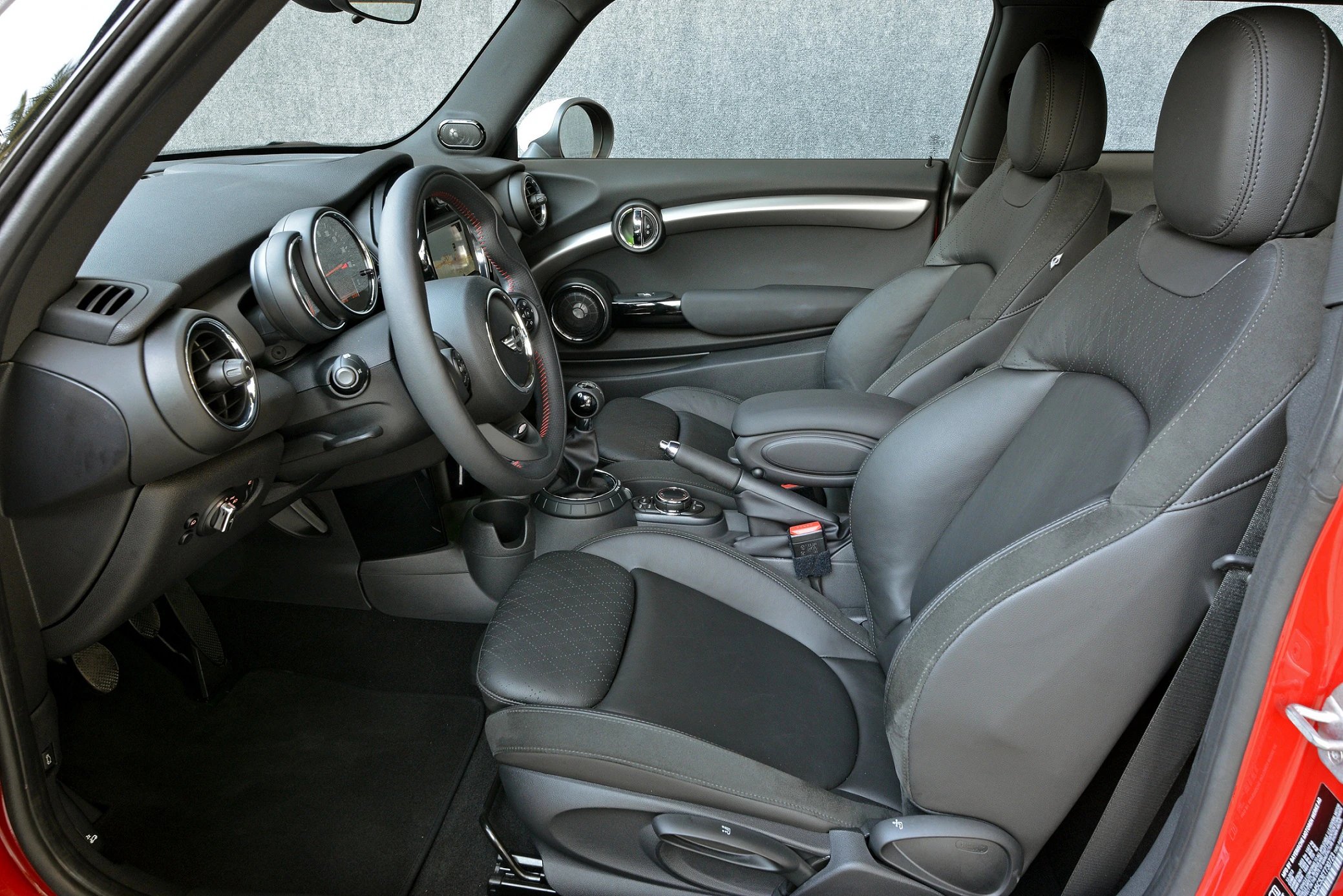 Innenraum eines modernen Autos mit grauen Ledersitzen, stilvollem Armaturenbrett und sportlichem Lenkrad. Beifahrertür geöffnet.