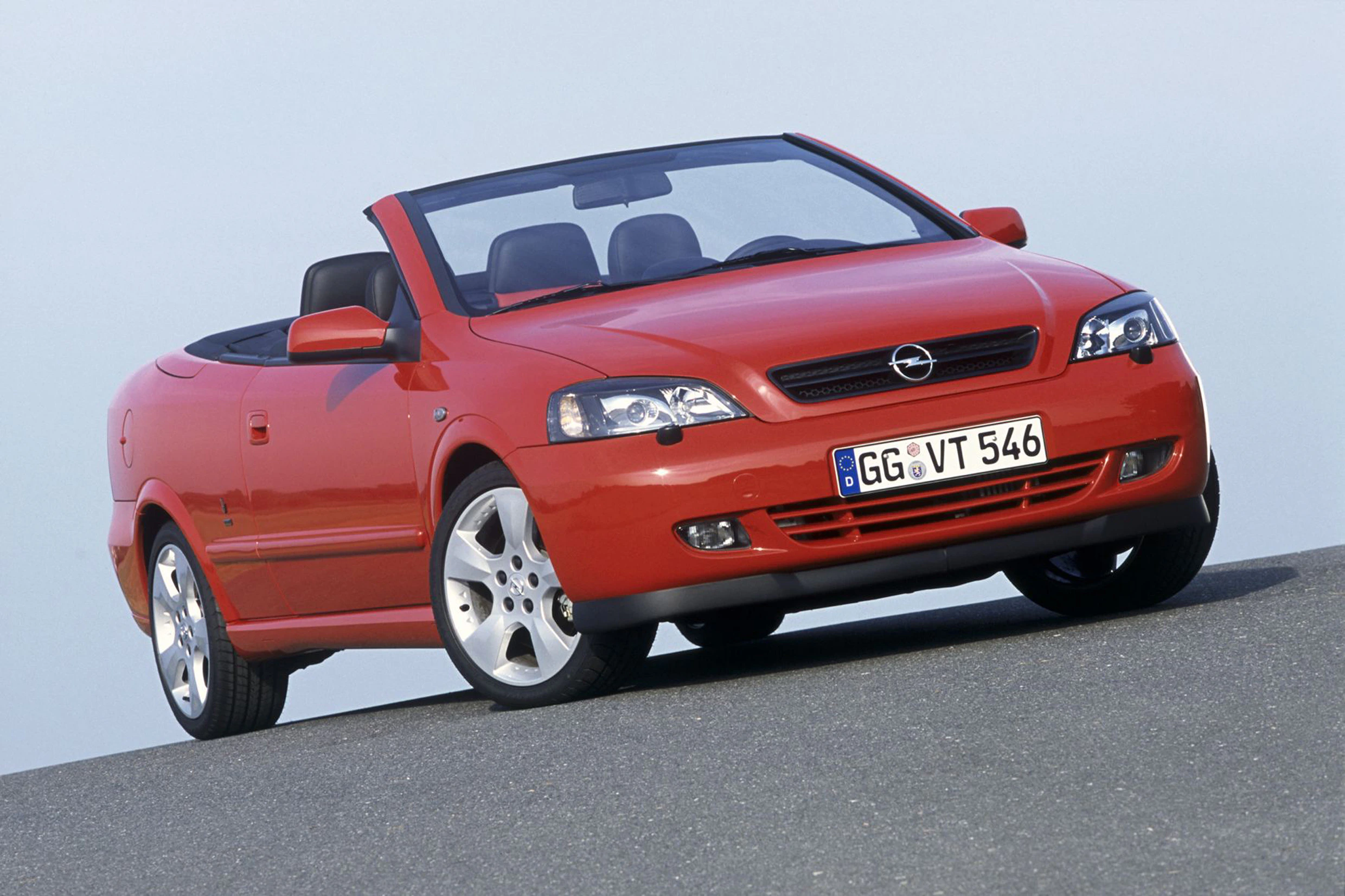 Rotes Opel Cabrio auf einer Straße, Vorderansicht. Klare Wetterbedingungen, der Himmel ist hell. Fahrzeug mit geöffnetem Verdeck.