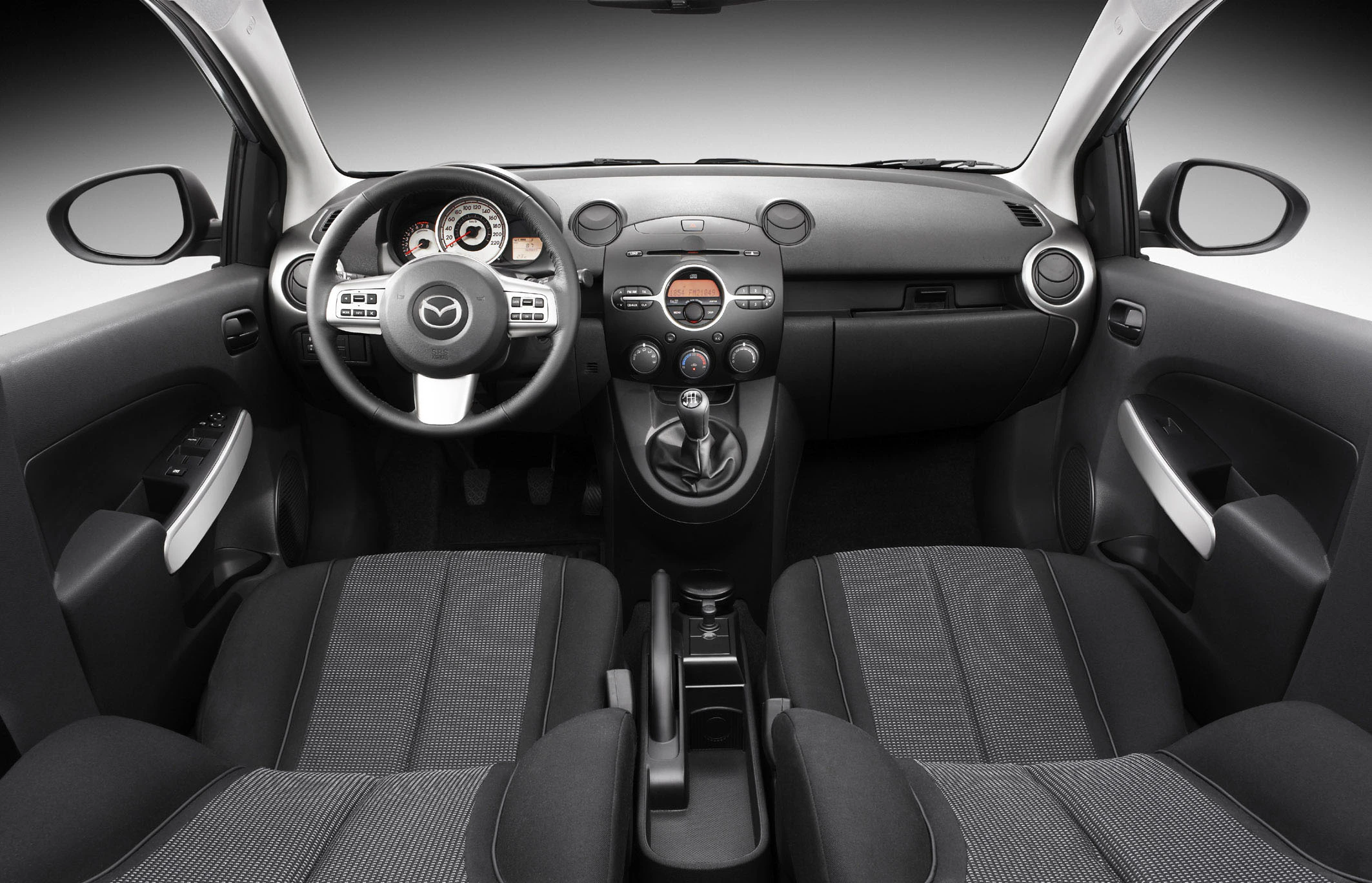 Innenraum eines Autos mit schwarzem Armaturenbrett, grauen Stoffpolstern, Rundinstrumenten und einem zentralen Schalthebel.