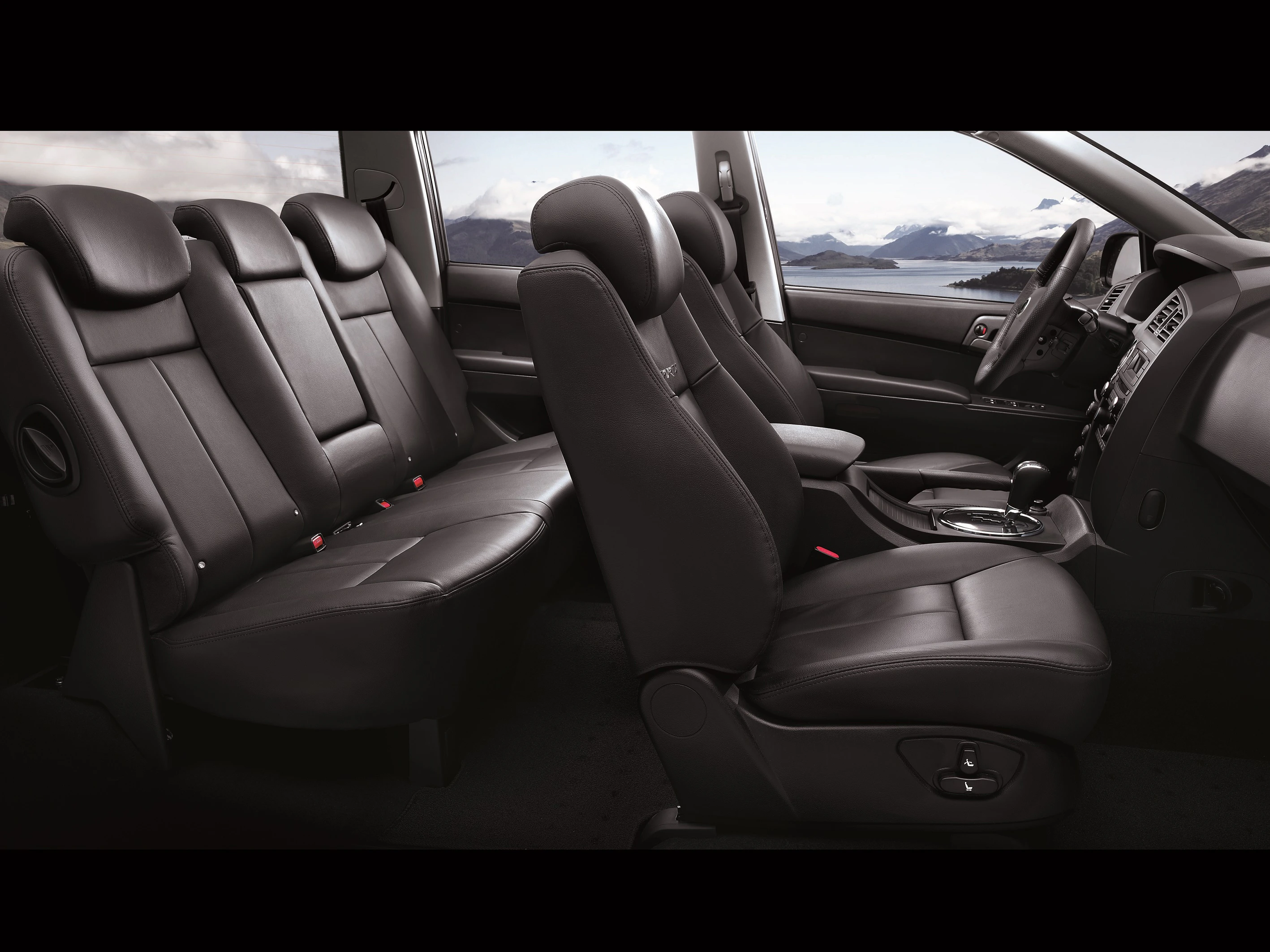 Innenraum eines Autos mit schwarzen Ledersitzen, Landschaft mit Bergen und Wasser im Hintergrund, zeigt geräumiges, modernes Design.
