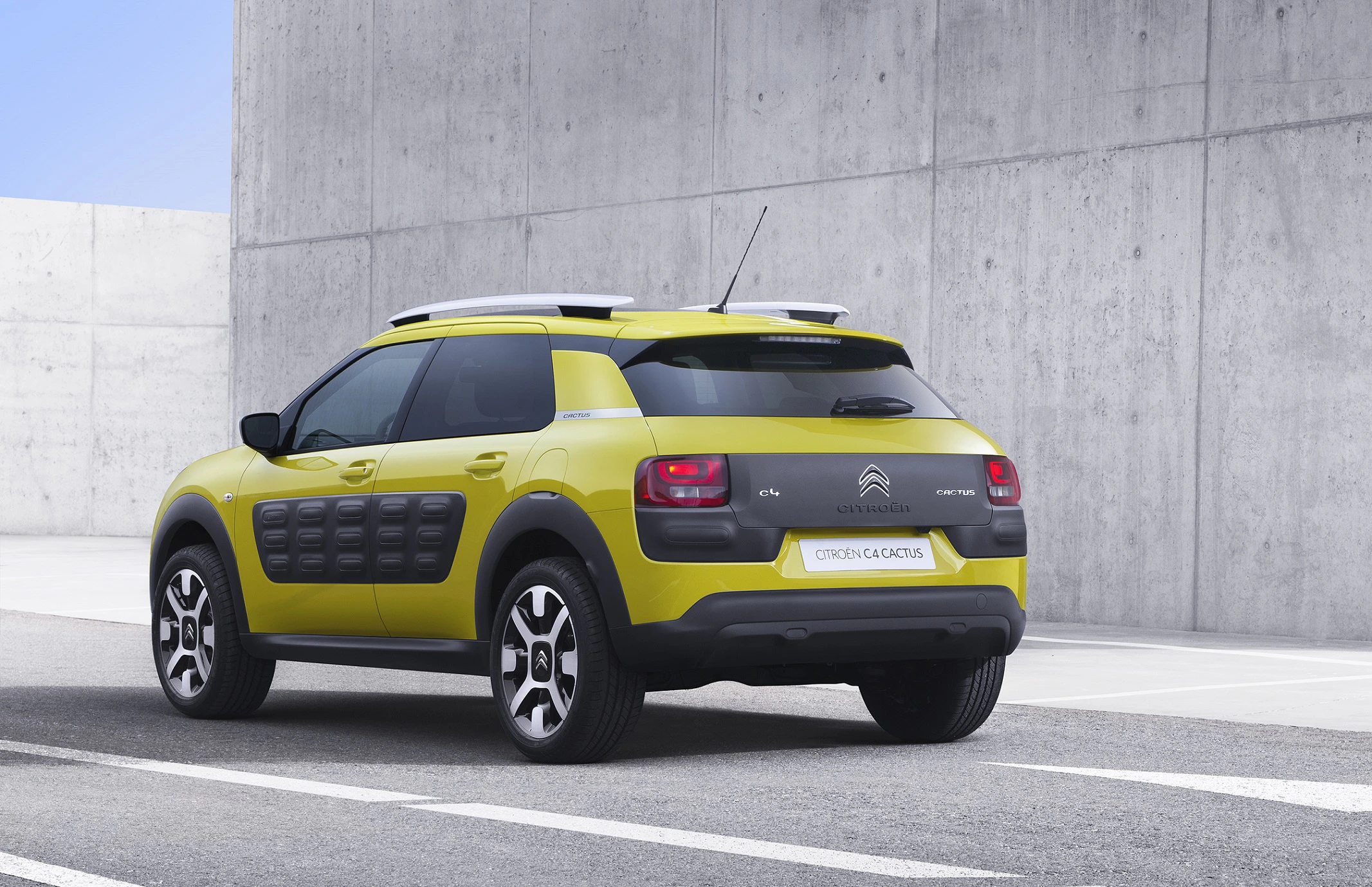 Gelber Citroën C4 Cactus mit markanten schwarzen Seitenelementen, geparkt vor einer Betonwand auf einer asphaltierten Fläche.