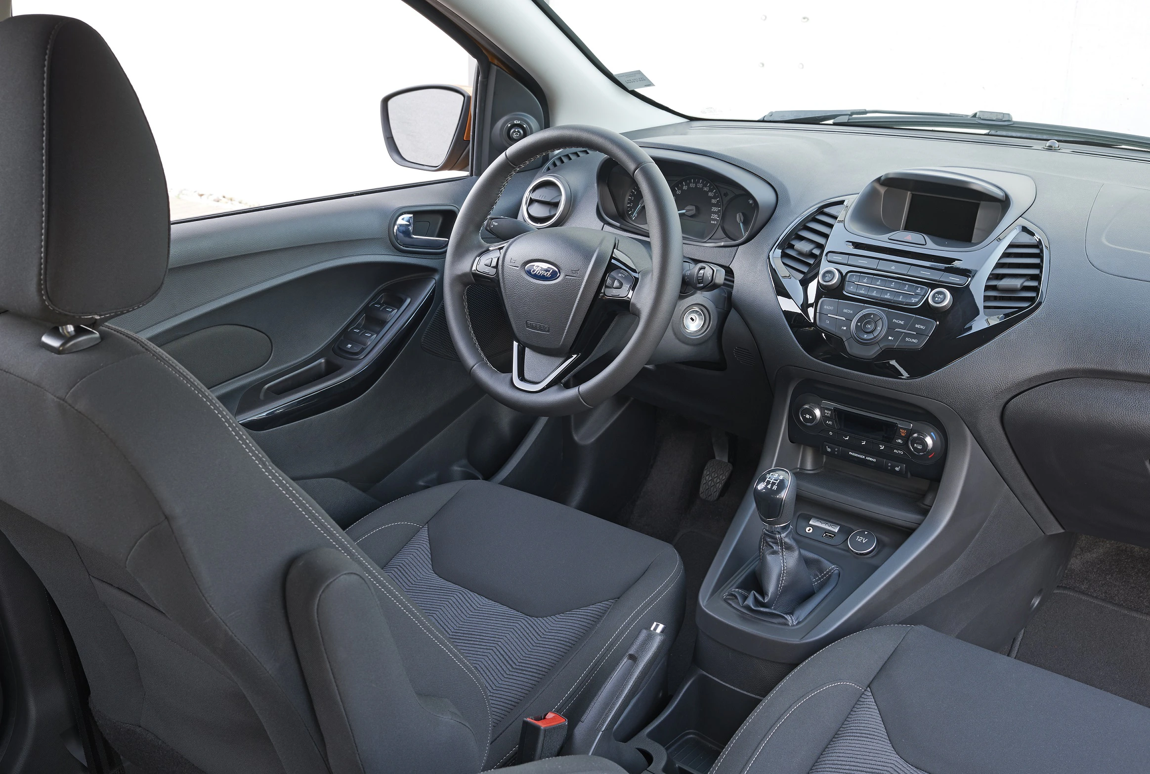 Innenraum eines Autos mit schwarzem Lenkrad, Schalthebel und dunklen Sitzen. Armaturenbrett mit Anzeigen und Belüftung.