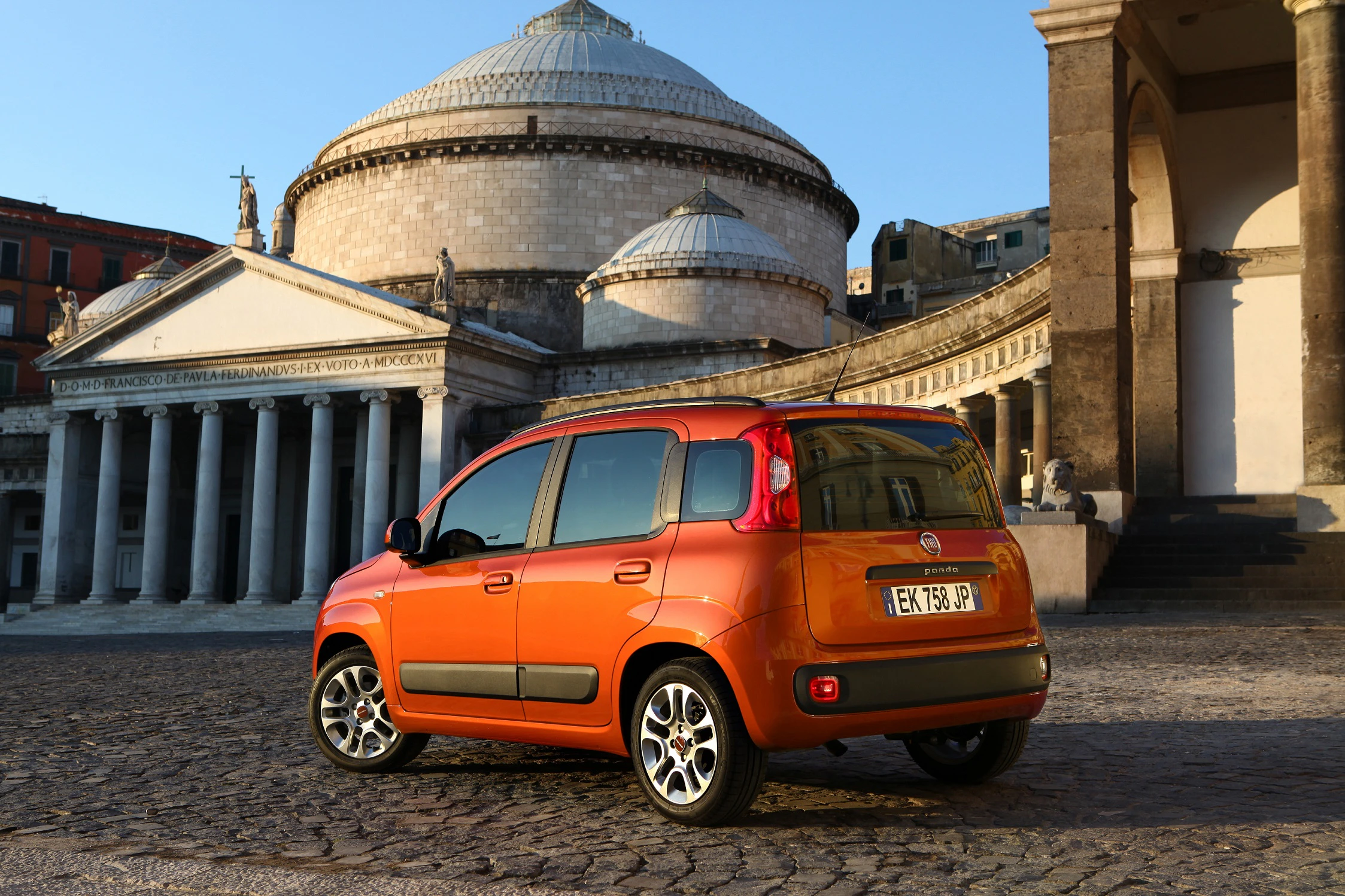 Oranger Fiat Panda in historischer Pflastersteinumgebung vor einer Kulisse klassischer Architektur mit Kuppel und Säulen.