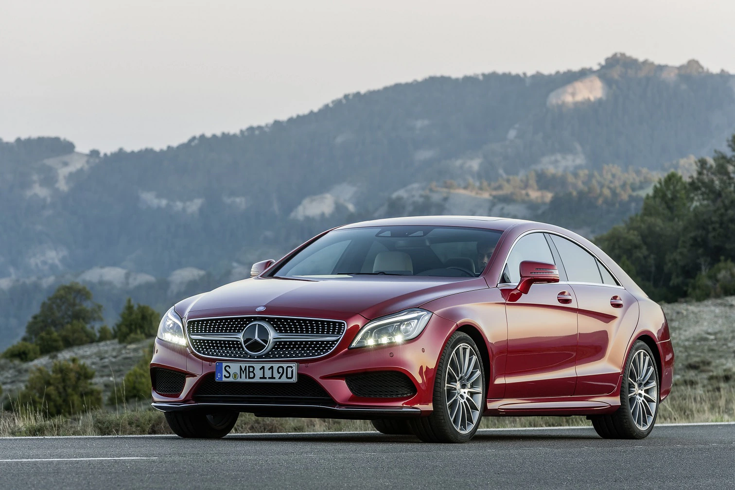 Roter Mercedes-Benz vor einer Bergkulisse auf einer Straße bei Tageslicht.