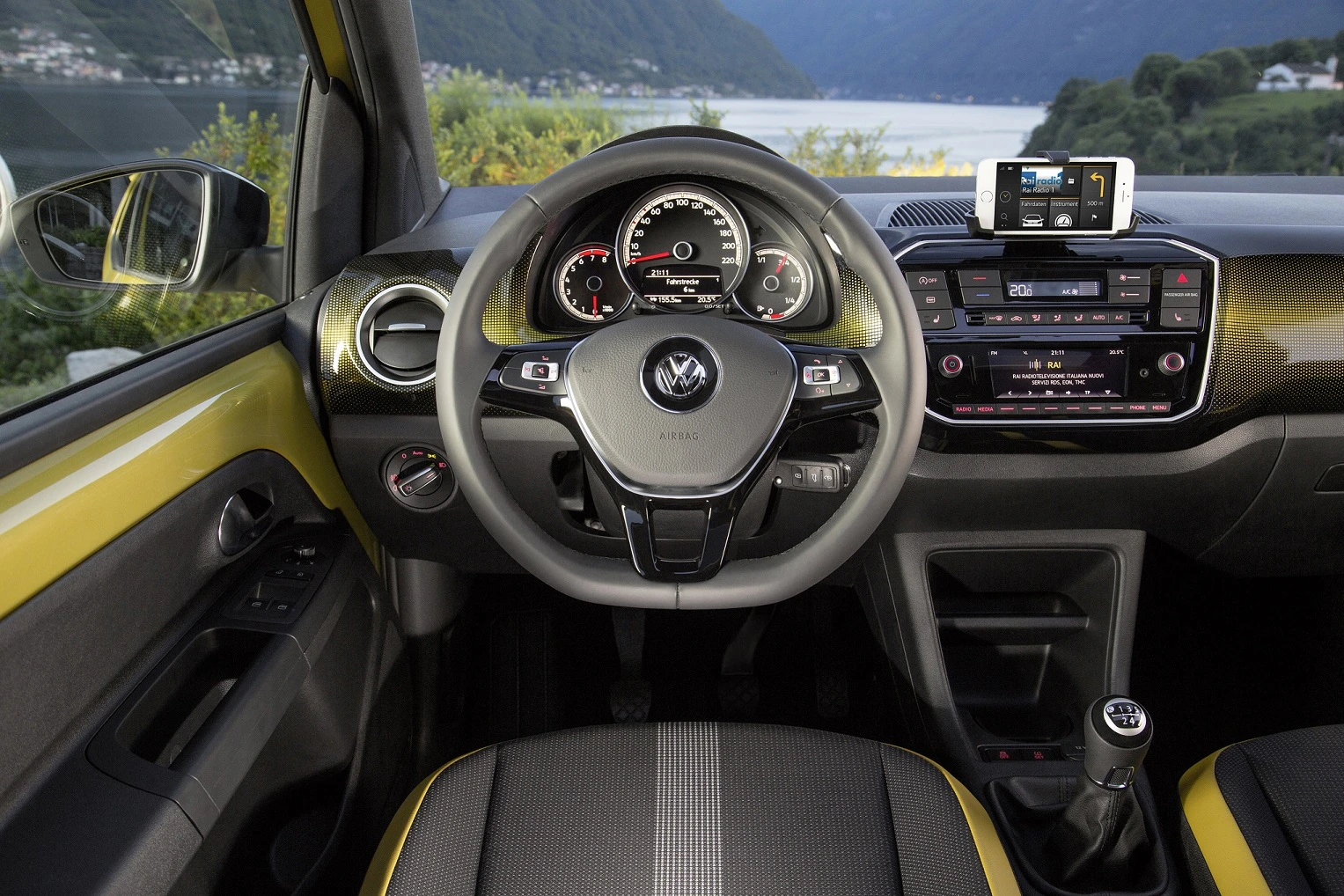 Lenkrad und Armaturenbrett eines Volkswagen mit eingebautem Navigationssystem und Blick auf einen See und Berge im Hintergrund.
