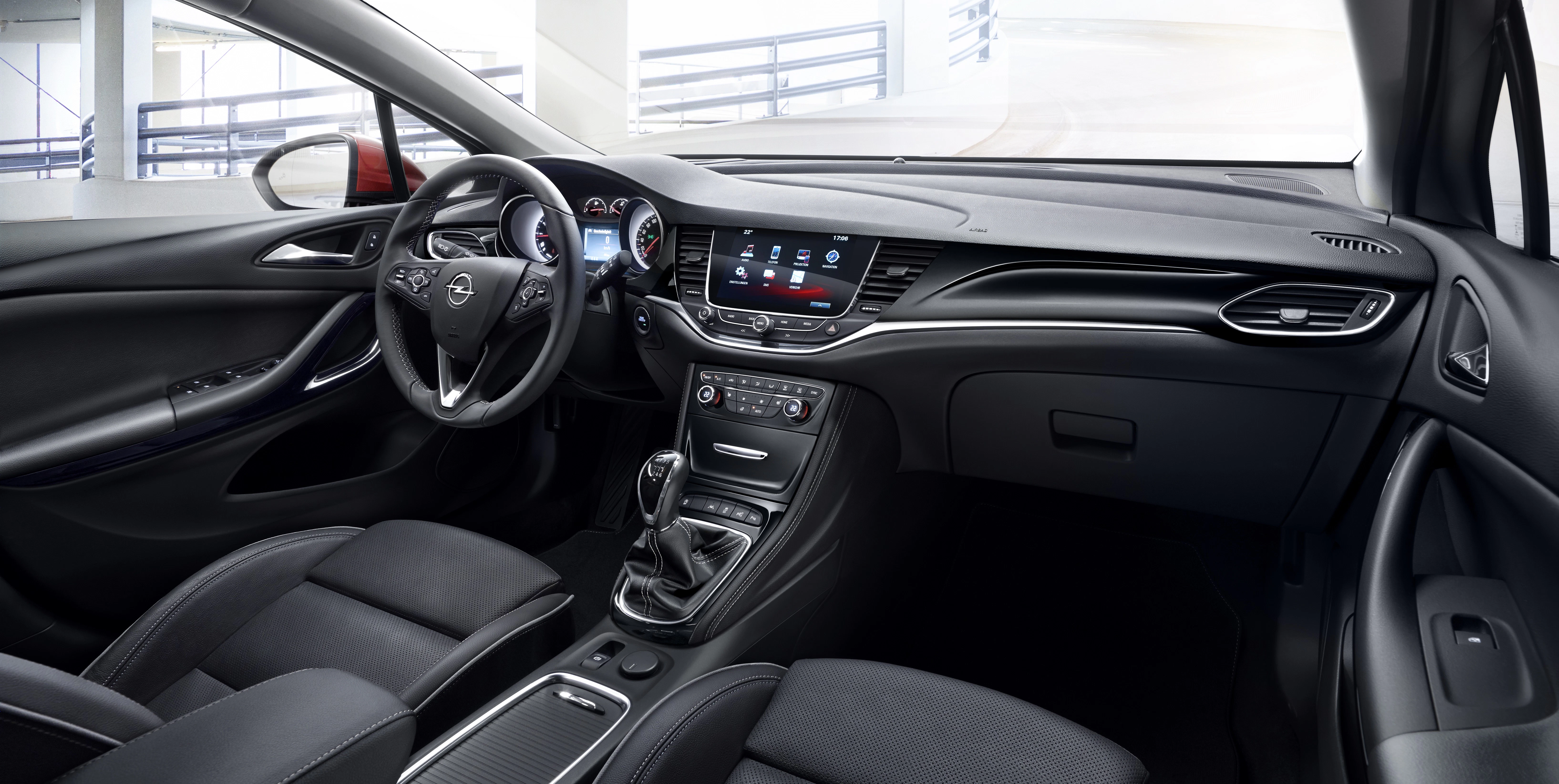 Innenraum eines modernen Autos mit Lederpolstern, Touchscreen-Display, Lenkrad mit Steuerungen und Schalthebel in einer Garage.