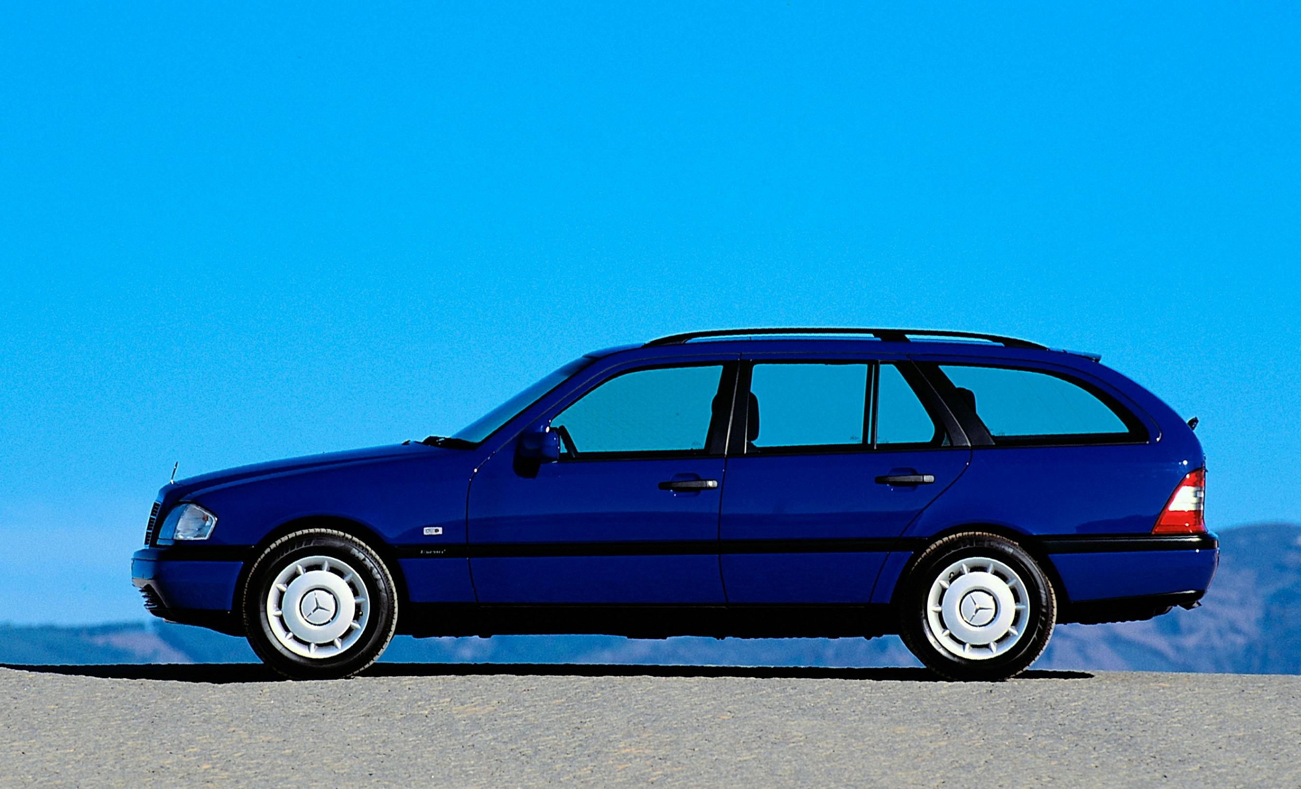 Blauer Kombi auf einer Straße vor einem klaren blauen Himmel, seitlich fotografiert. Im Hintergrund sind undeutliche Berge zu sehen.