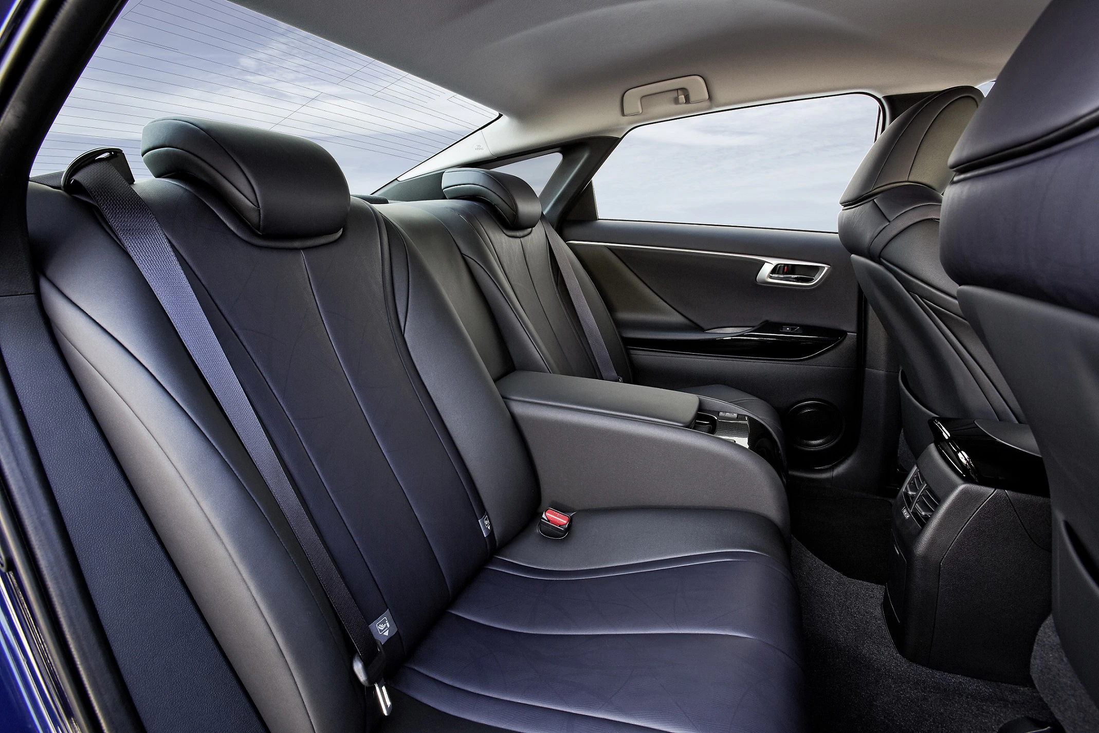Rückbank eines Autos mit schwarzen Ledersitzen, Sicherheitsgurten und Mittelarmlehne vor einem Fenster mit sichtbarem Himmel.