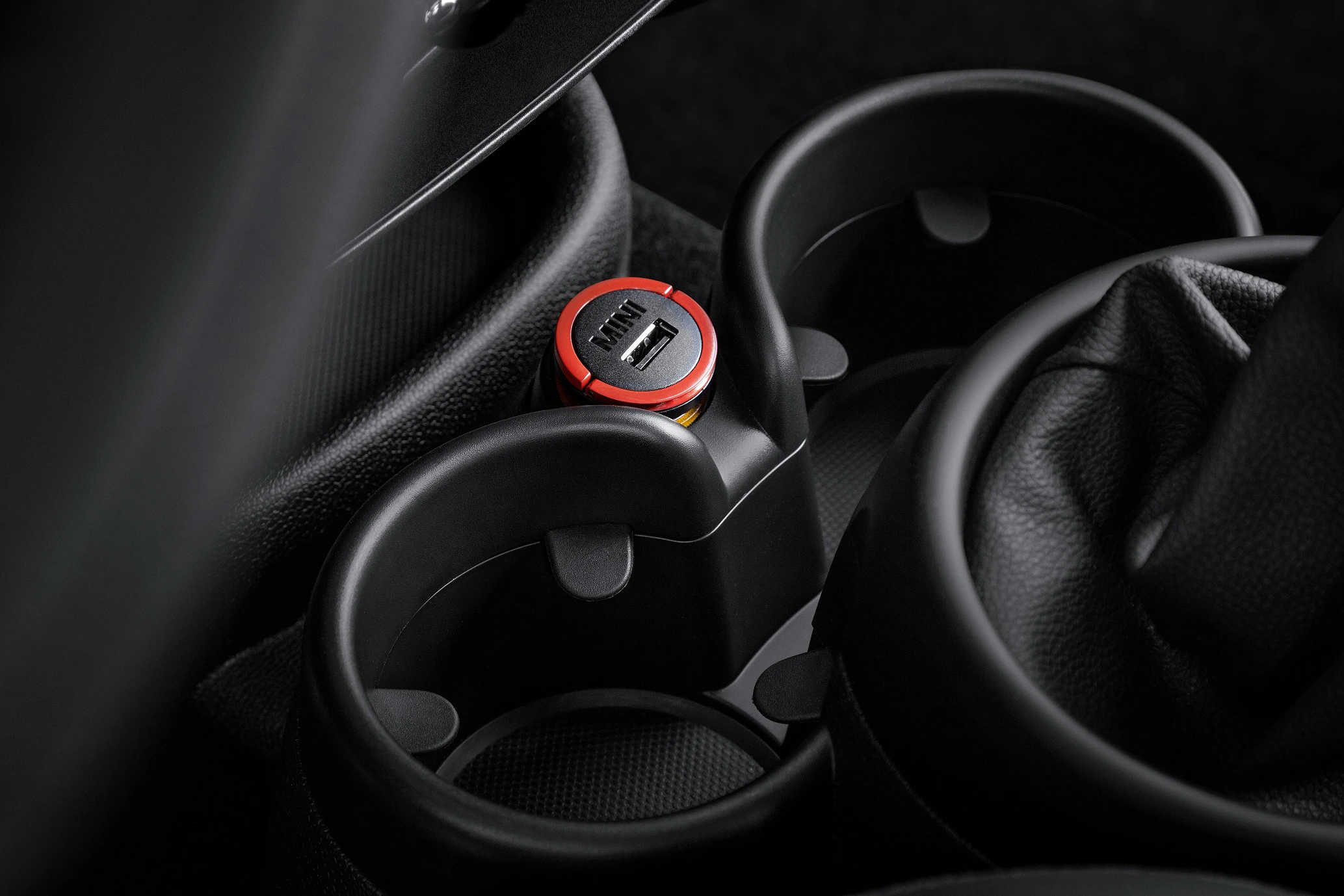 Getränkehalter mit USB-Ladeanschluss in einem Auto, umgeben von schwarzem Polstermaterial.