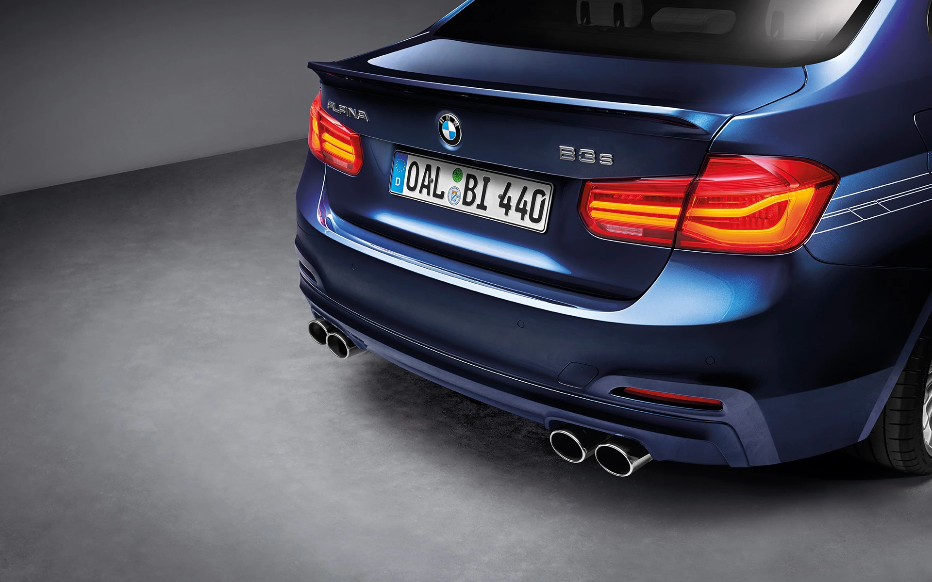 Blauer BMW Alpina mit sichtbarem Kennzeichen „OAL BI 440“, beleuchteten Rücklichtern und Doppelauspuff, von hinten fotografiert.