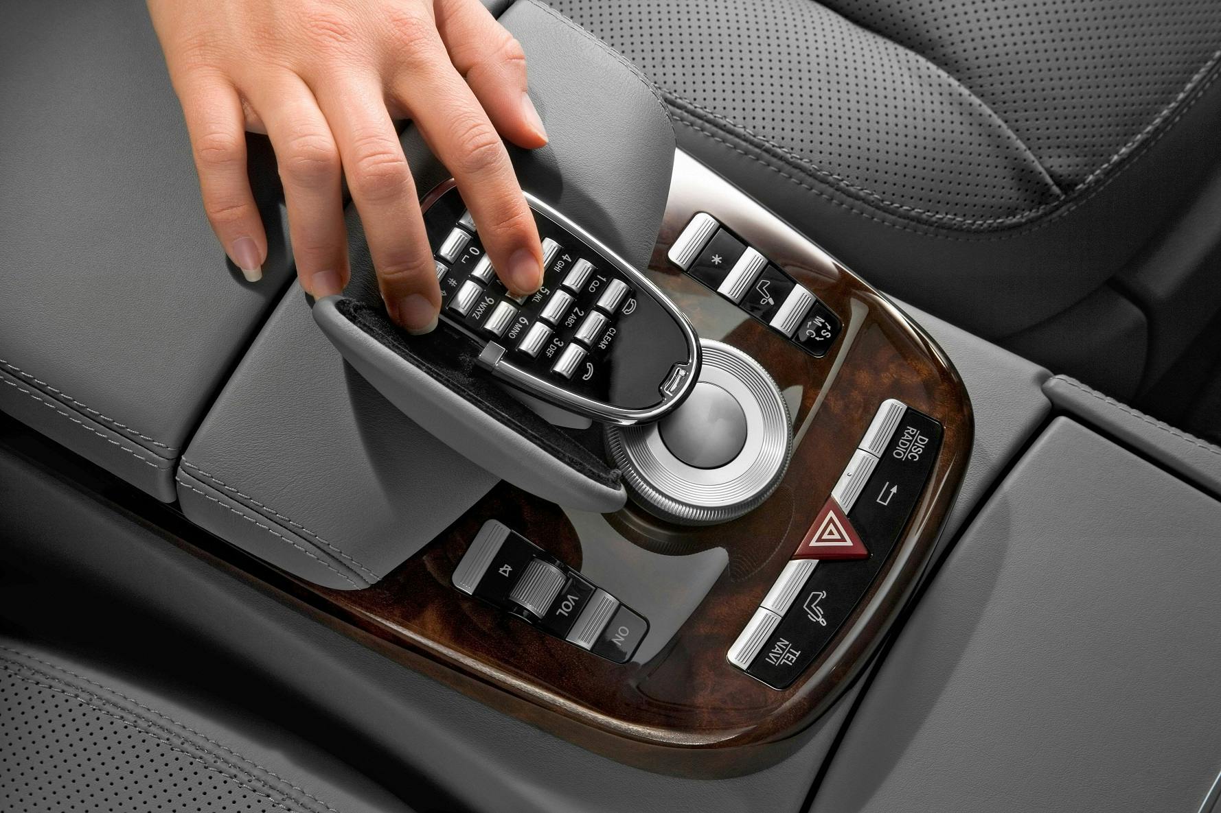 Hand bedient Autokonsole mit Tastenfeld, Drehregler und Holzdekor.