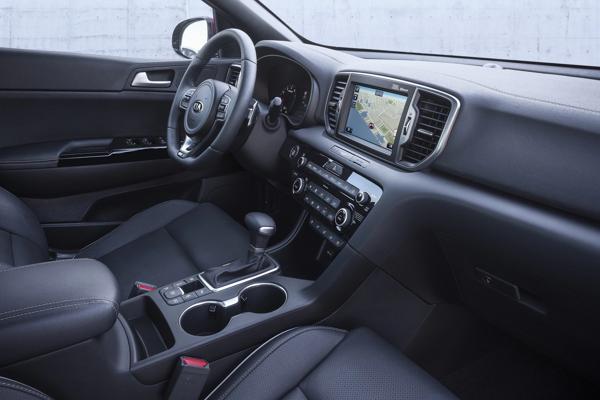 Innenraum eines modernen Autos mit Touchscreen-Display, Lenkrad, Schalthebel und schwarzen Ledersitzen.