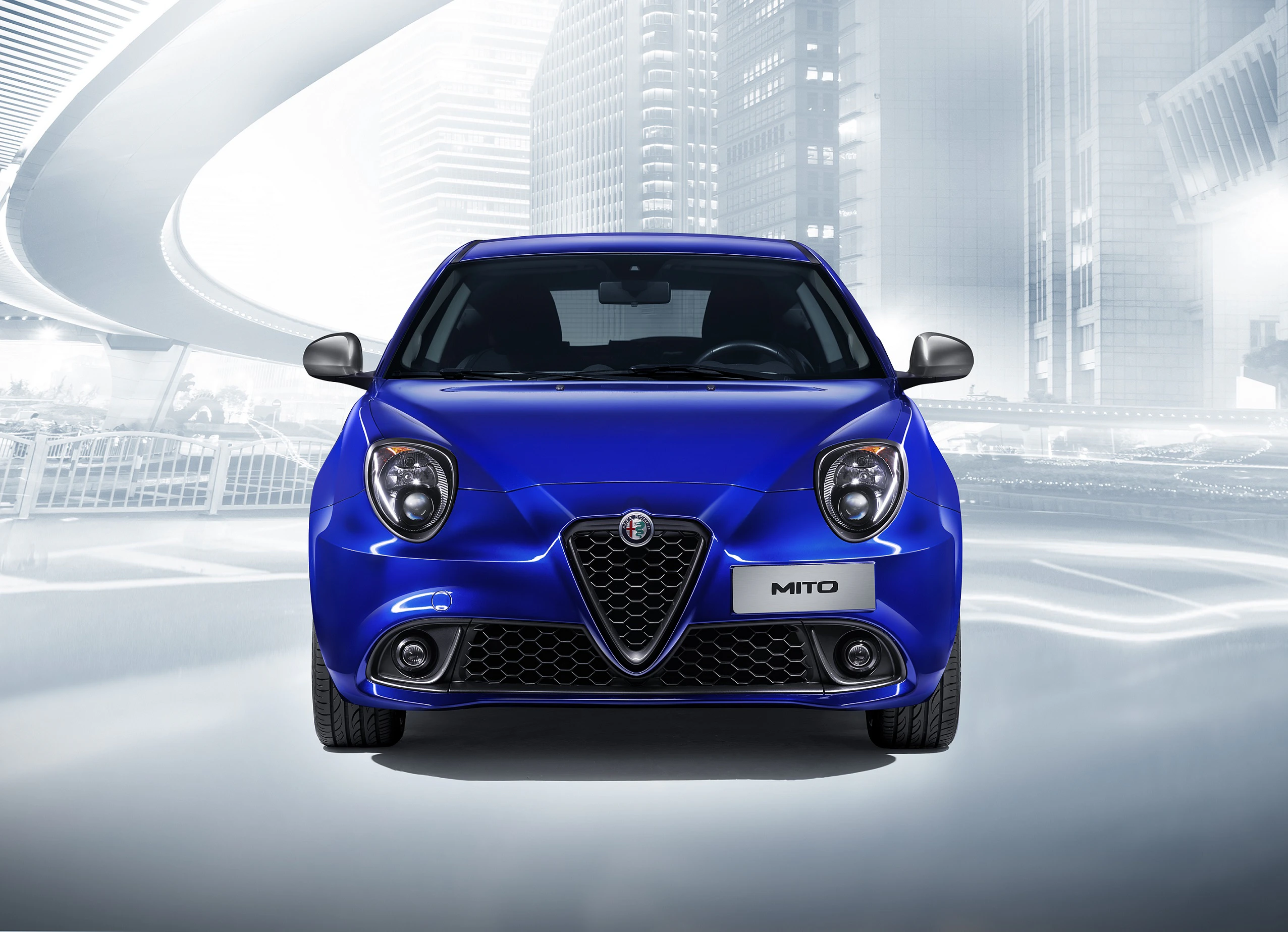Blauer Alfa Romeo Mito, Frontansicht, vor futuristischer Stadtlandschaft mit geschwungenen Brücken und modernen Gebäuden.