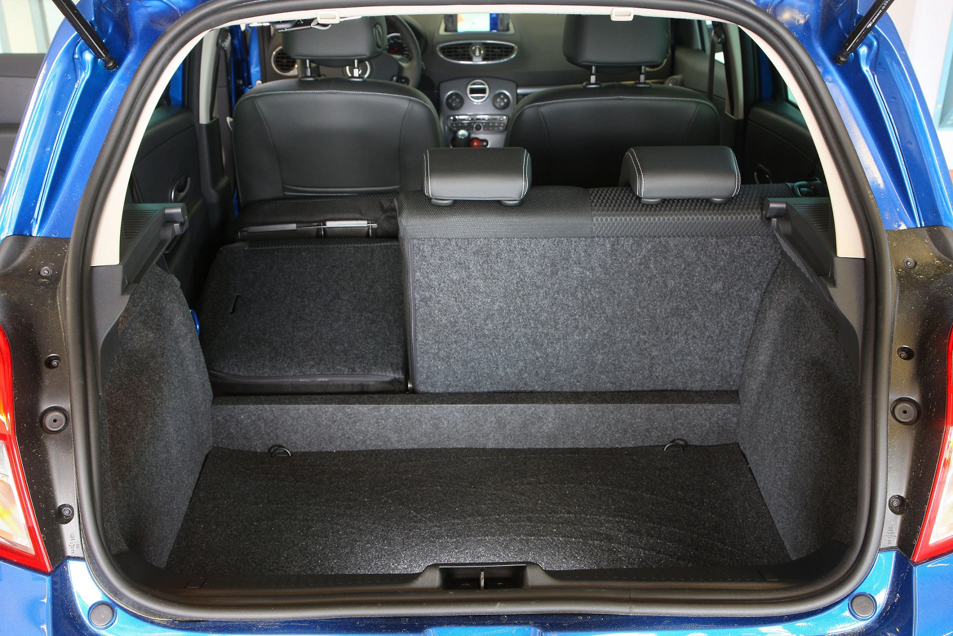 Blauer Kleinwagen mit geöffnetem Kofferraum, Rücksitz teilweise umgeklappt, grauer Teppichboden, Blick in den Innenraum.