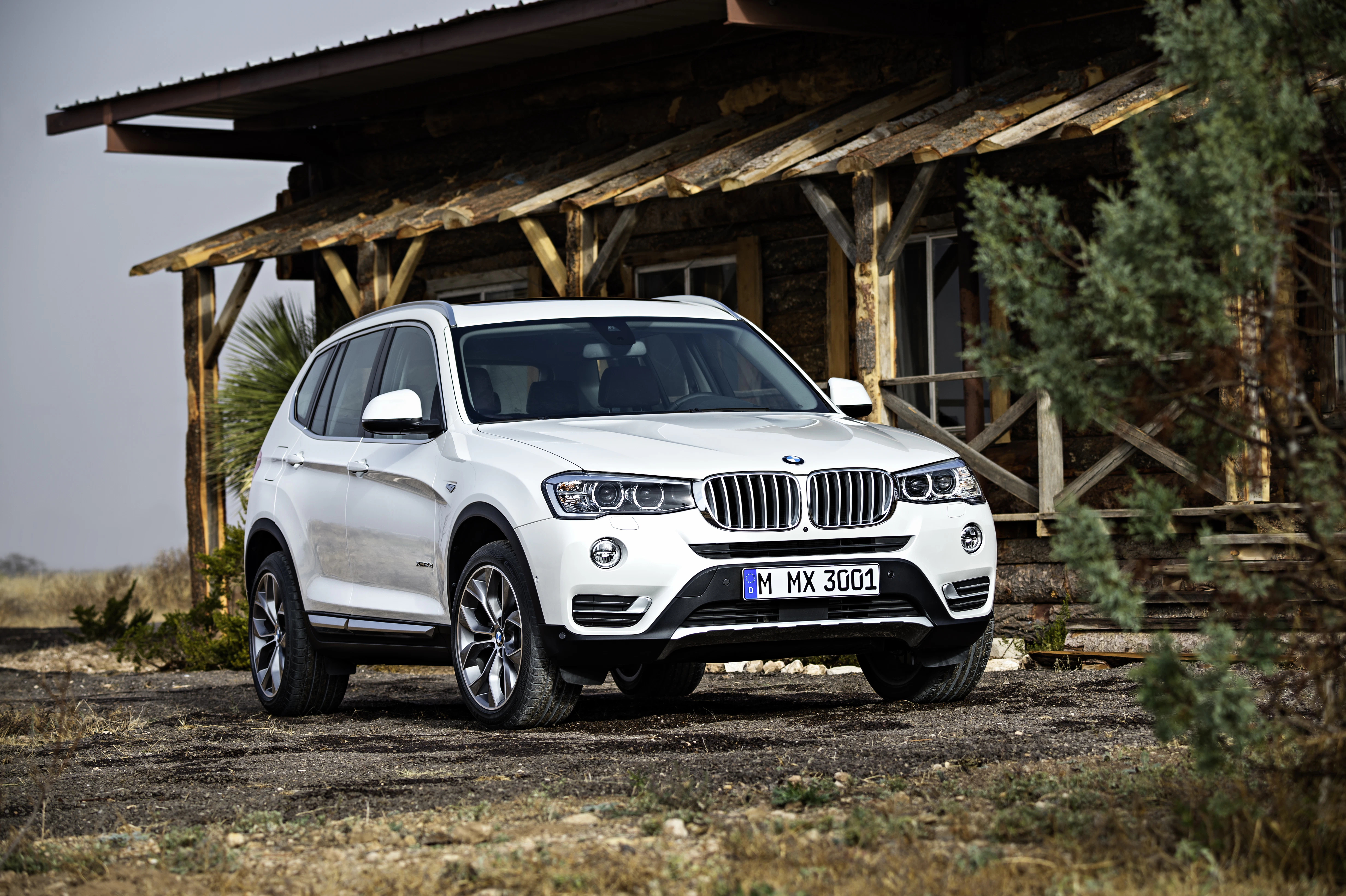 Weißer SUV parkt vor einer rustikalen Holzhütte in einer natürlichen, trockenen Umgebung.