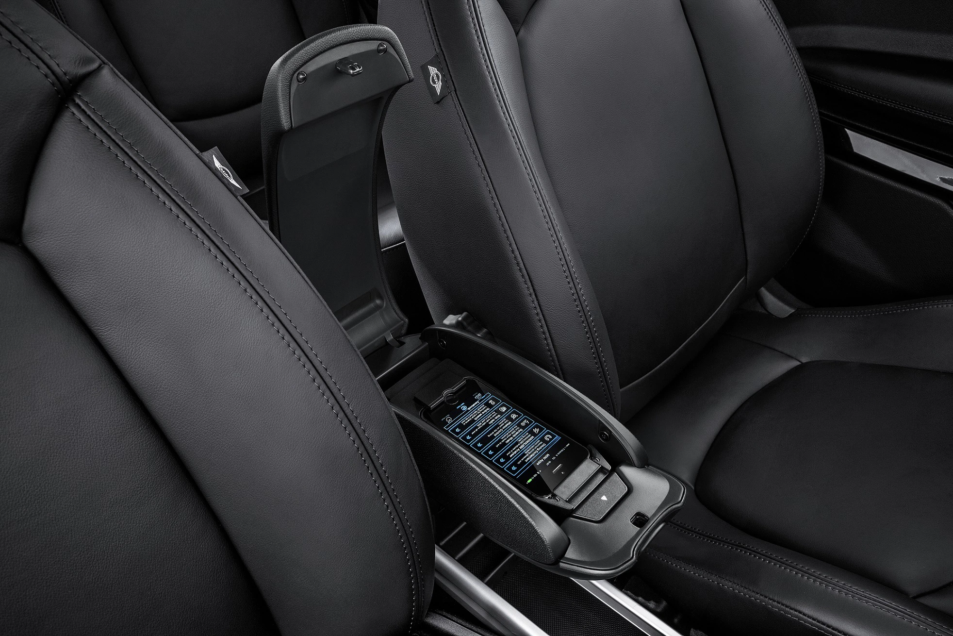 Schwarze Autositze mit geöffnetem Mittelarmlehnenfach, das ein Smartphone mit einem beleuchteten Display enthält.