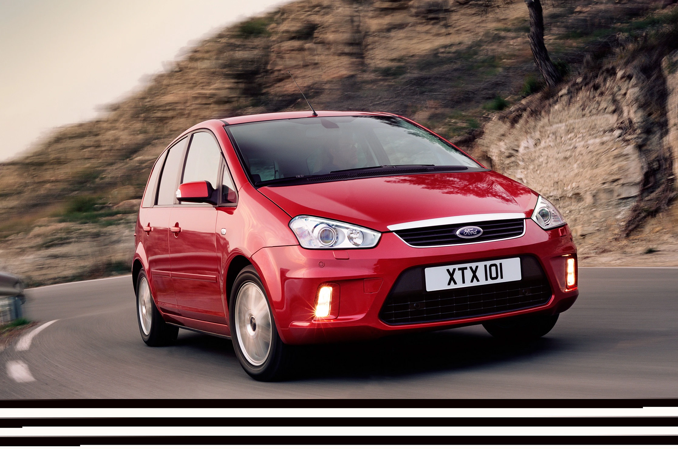 Roter Ford C-Max fährt in einer scharfen Kurve. Dynamische Landschaft im Hintergrund, Fokus auf das Auto.