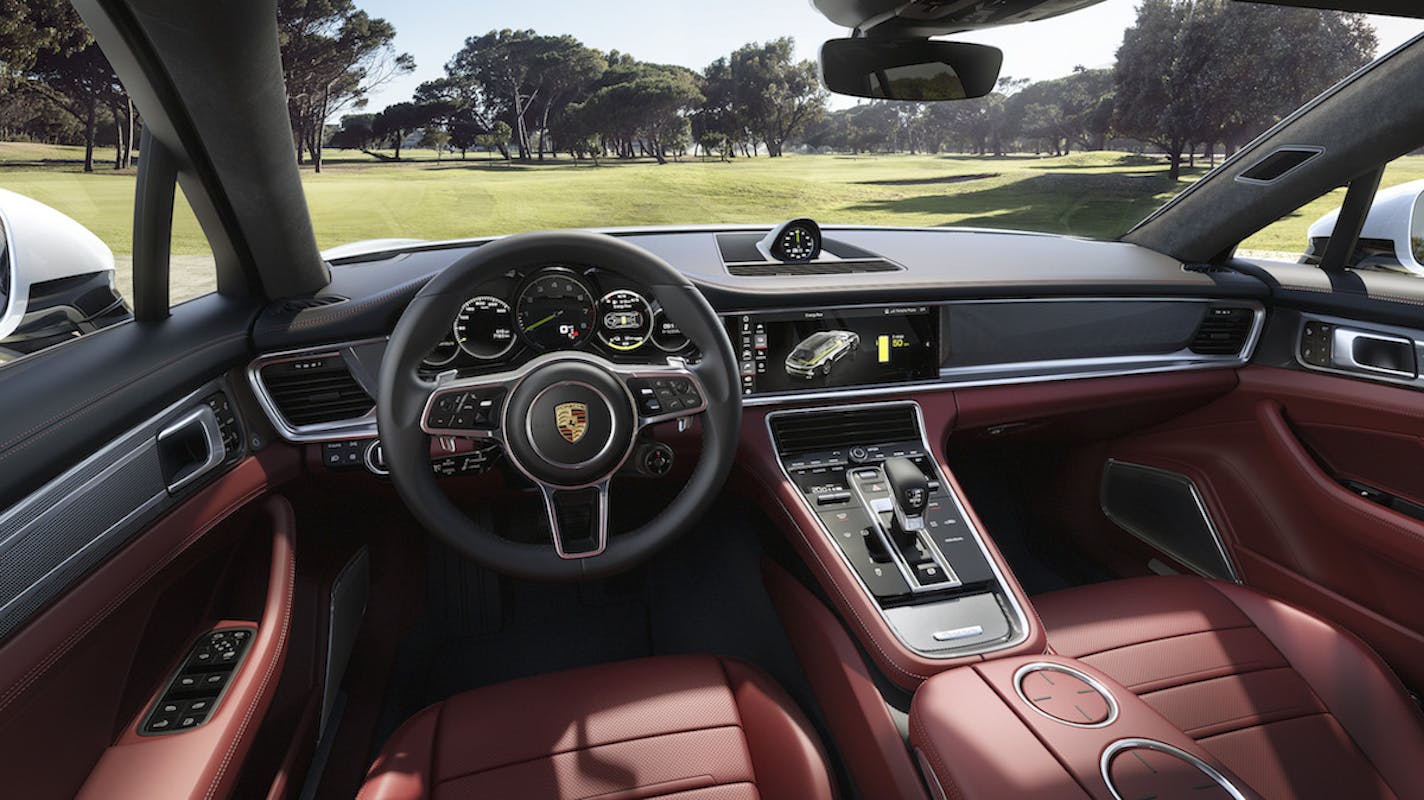 Innenansicht eines Autos mit roter Innenausstattung und moderner Armatur. Ein grüner Golfplatz ist durch die Windschutzscheibe sichtbar.