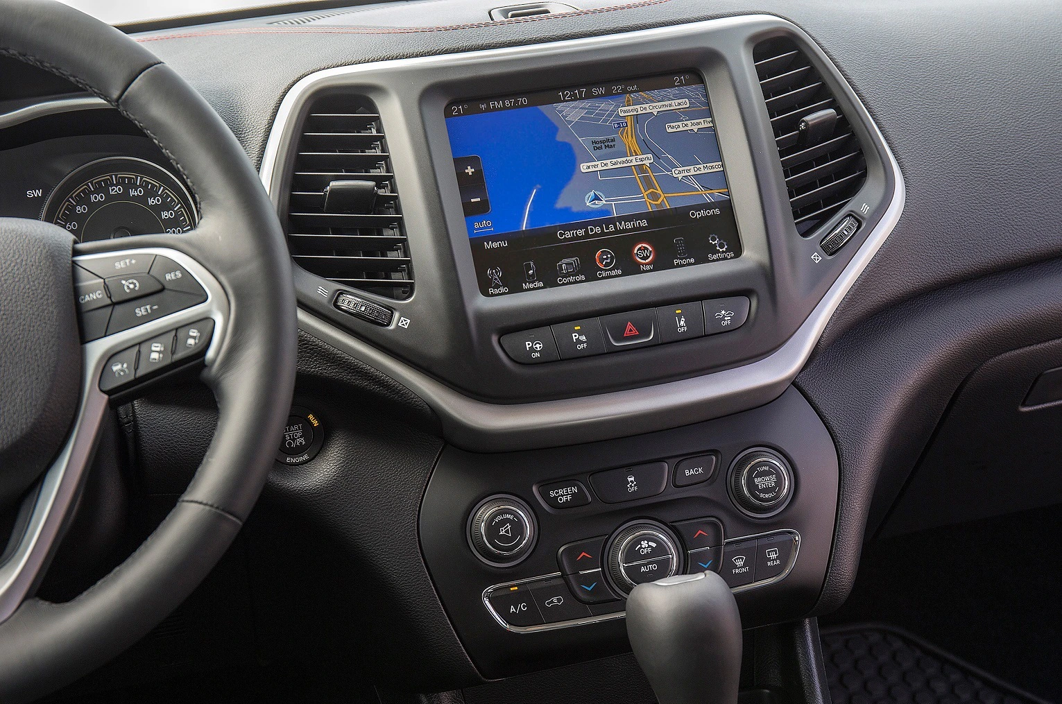 Lenkrad und Armaturenbrett eines Autos mit eingebautem Navigationssystem auf dem Bildschirm, umgeben von Bedienelementen.