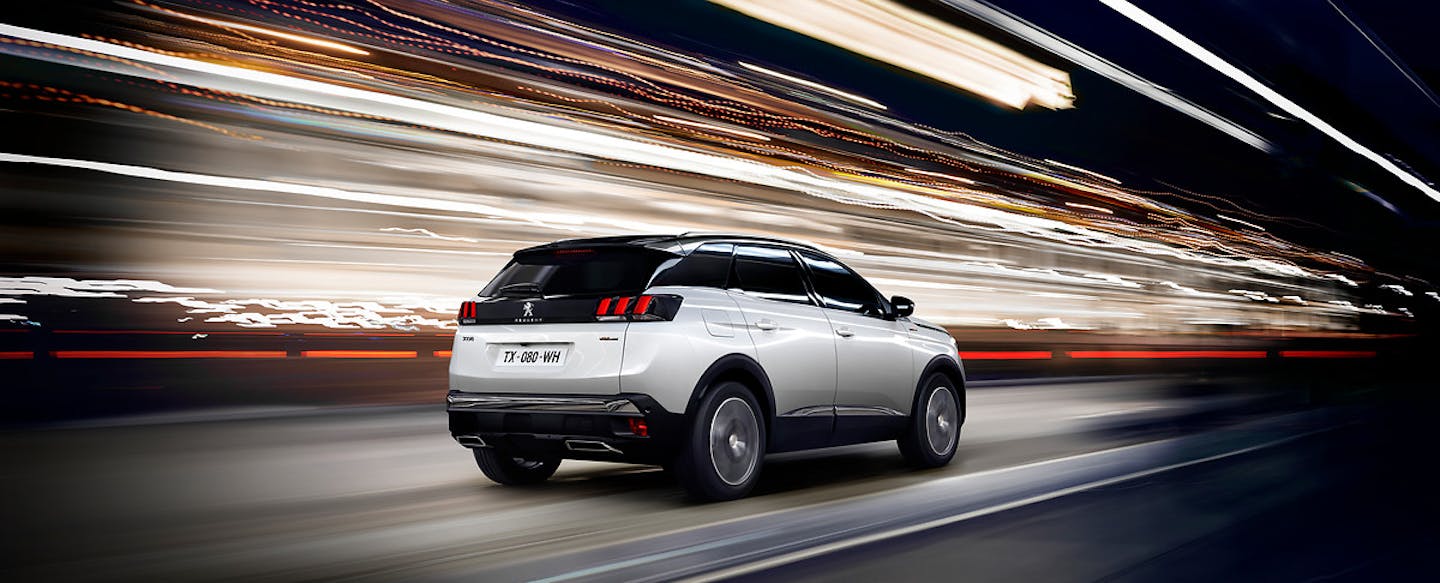 SUV fährt nachts auf beleuchteter Straße, erzeugt dynamischen Effekt durch Lichtstreifen.