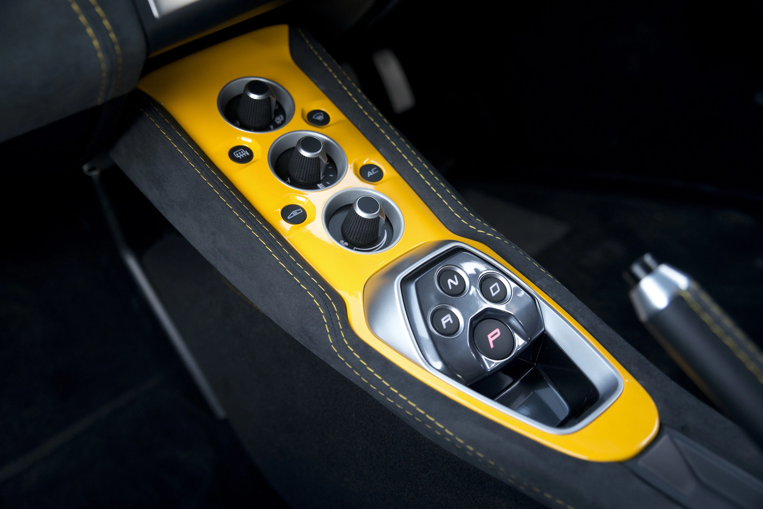 Nahaufnahme einer Mittelkonsole in einem Auto mit gelber Verkleidung; enthält Drehregler und einen Schaltknopf mit Optionen N, R und P.