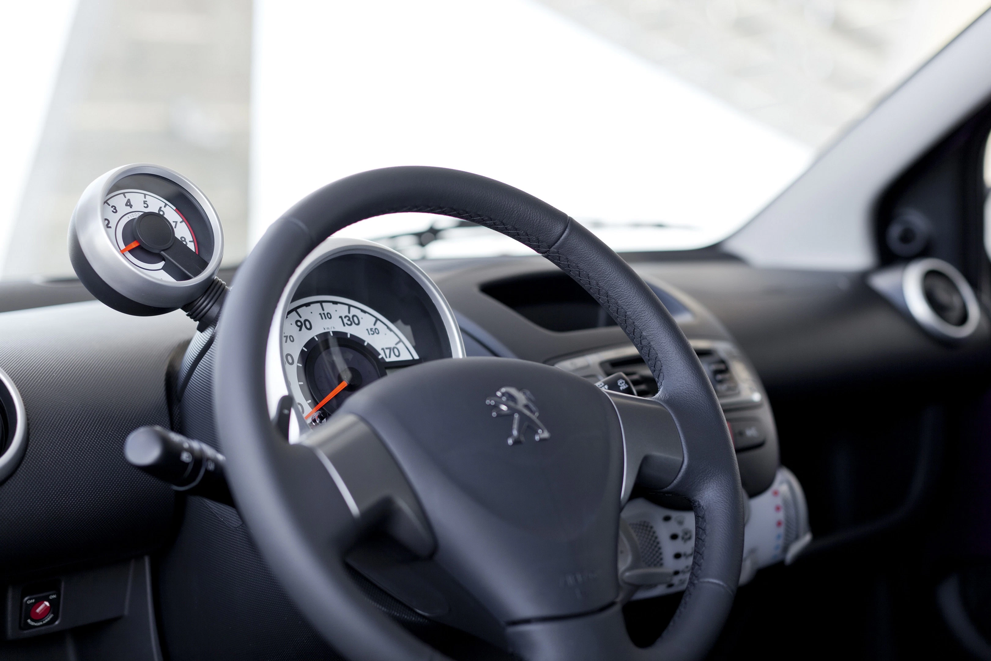 Innenraum eines Autos mit Blick auf das Lenkrad, Tachometer und Armaturen. Das Peugeot-Logo ist auf dem Lenkrad zu sehen.