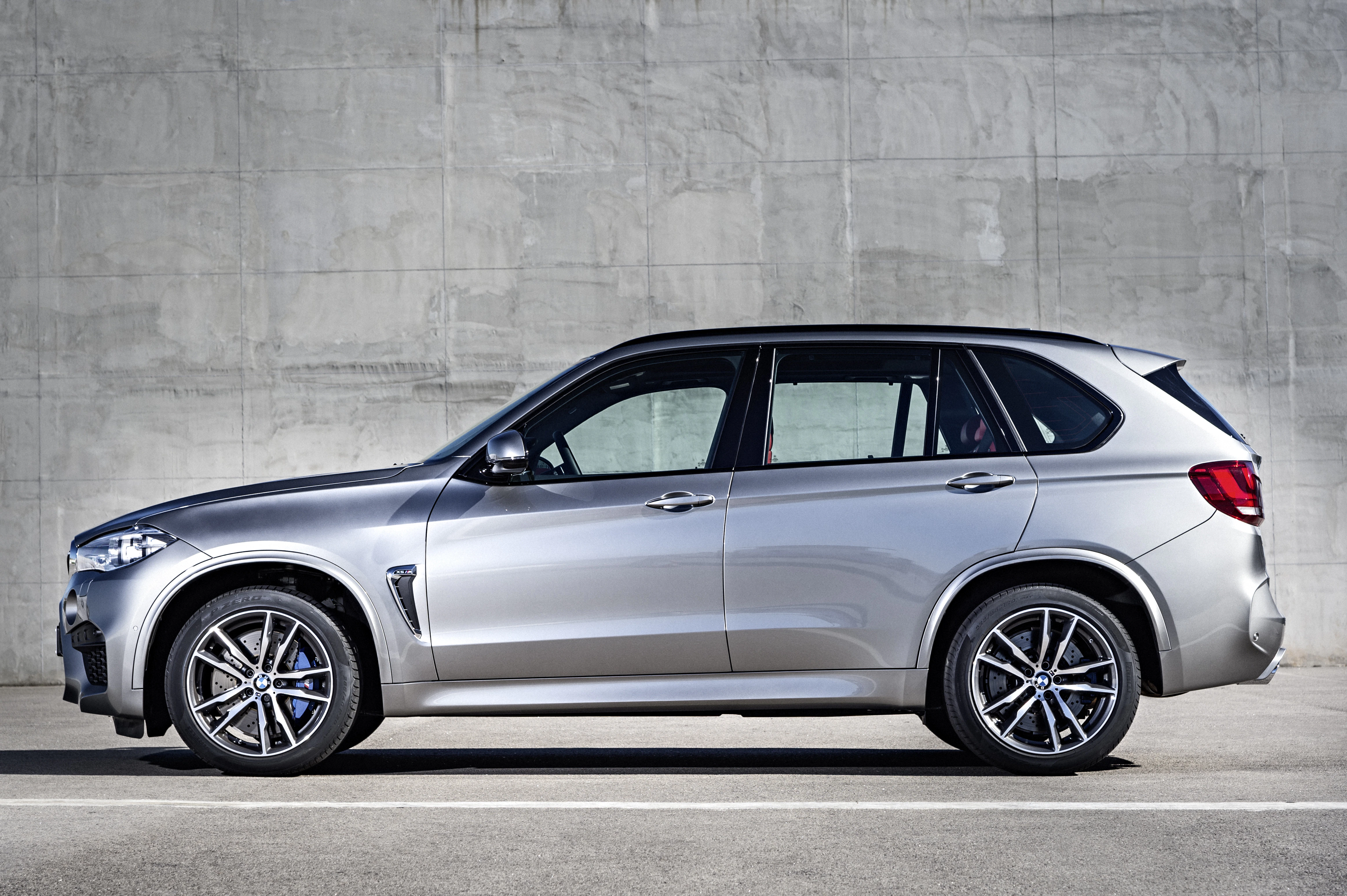 Silbernes SUV mit sportlichem Design, steht seitlich vor einer grauen Betonwand auf Asphalt. Moderne Leichtmetallräder sind sichtbar.