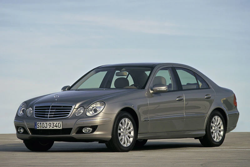 Silberner Mercedes-Benz E-Klasse Limousine mit glänzenden Felgen, geparkt auf grauem Asphalt vor blauem Himmel.