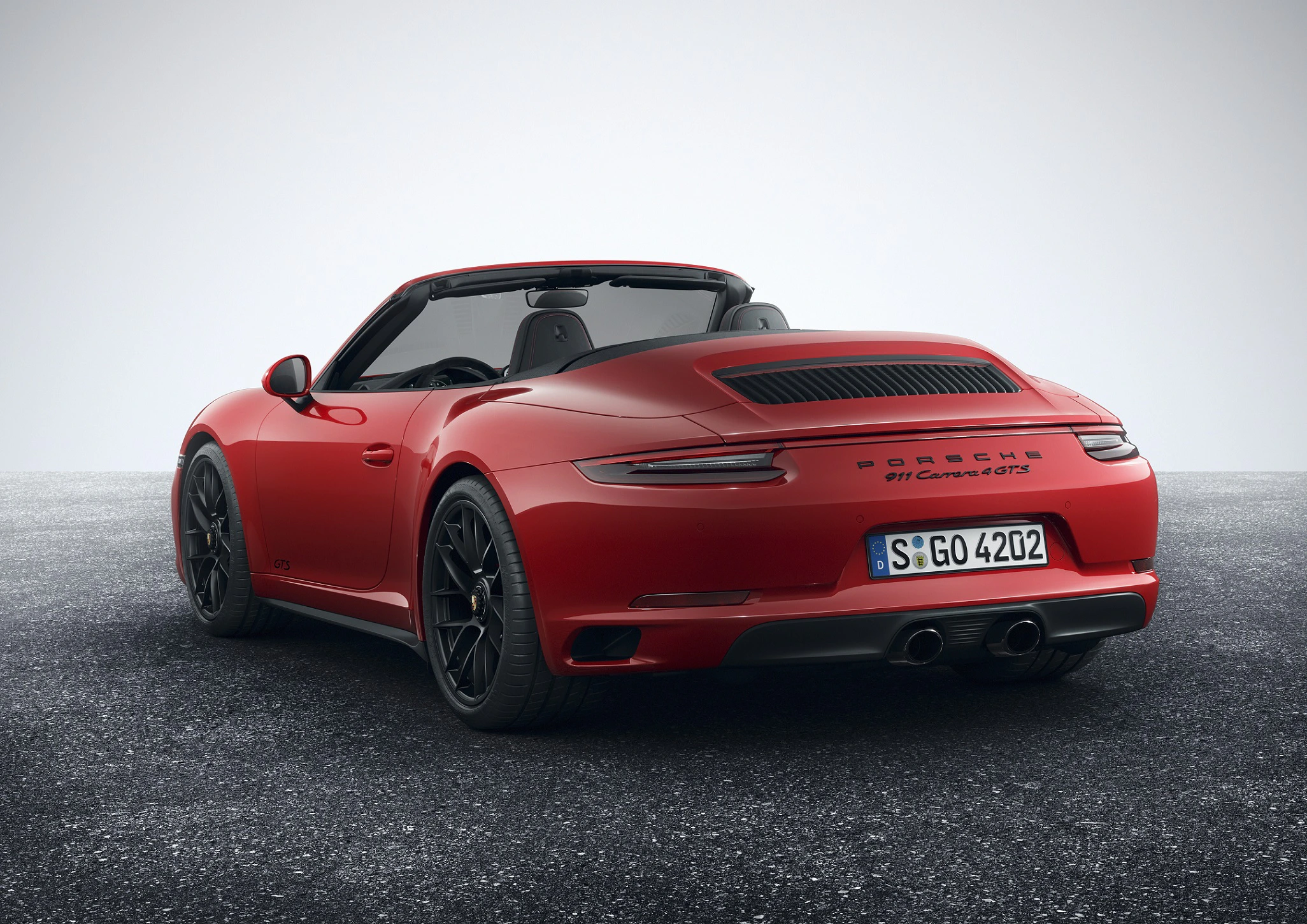 Rotes Cabriolet-Sportwagen mit offener Verdeckansicht auf grauem Asphalt, Rückansicht mit sichtbaren Rückleuchten und Auspuffrohren.
