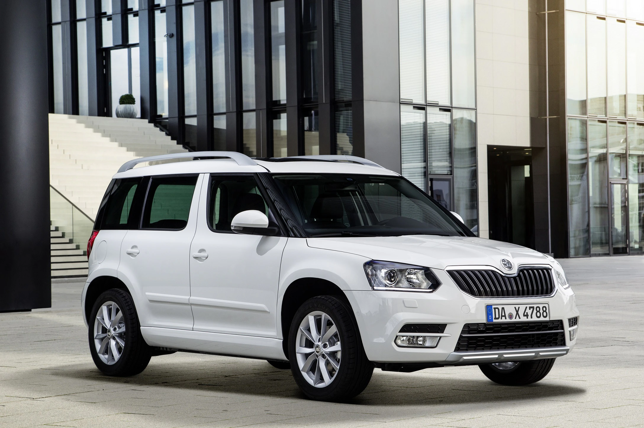 Weißer SUV der Marke Škoda, geparkt vor einem modernen Gebäude mit großen Fenstern und Treppe im Hintergrund.
