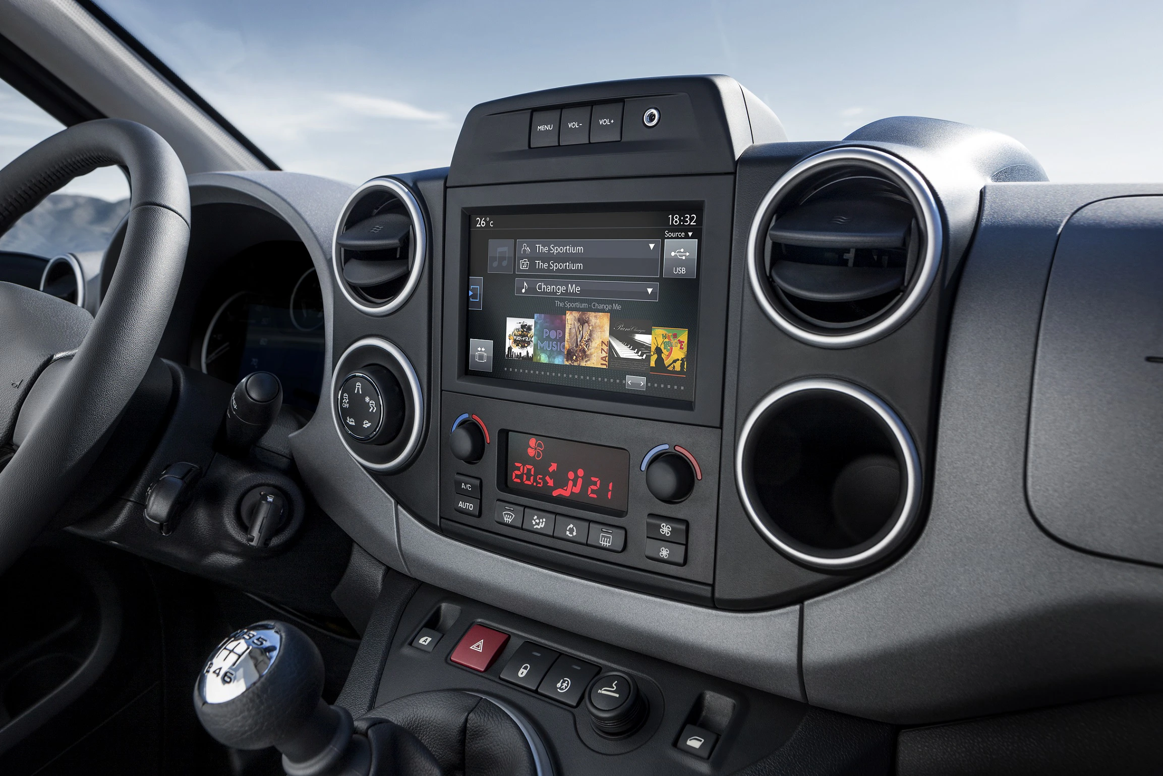 Nahaufnahme eines modernen Autoinnenraums. Zentraler Touchscreen zeigt Musik-Playlist an. Lüftungsdüsen und Steuerknöpfe sind sichtbar.