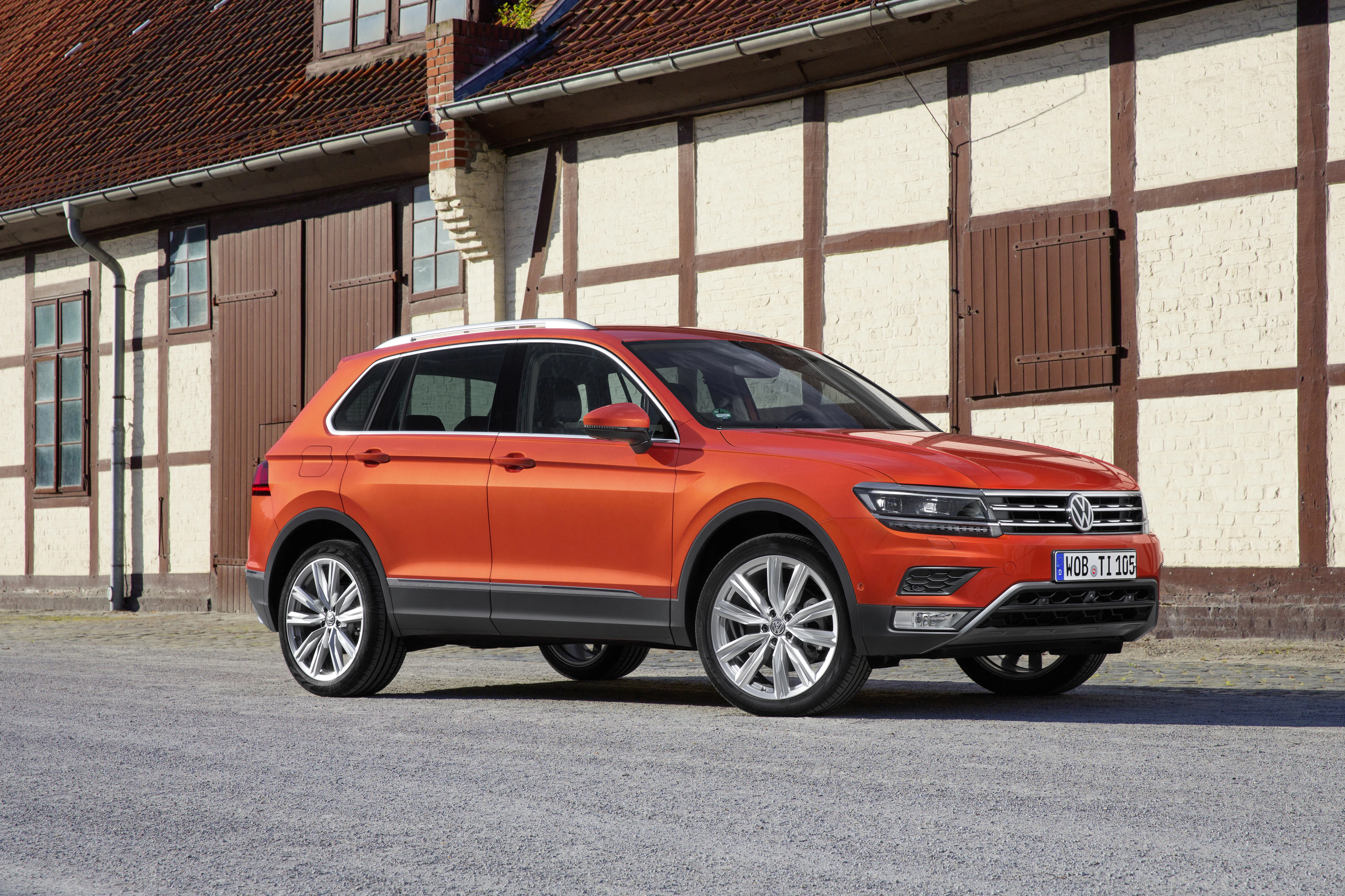 Orangefarbener SUV parkt vor einem Fachwerkhaus mit braunen Türen und Fenstern an einem sonnigen Tag.
