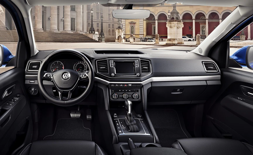 Innenraum eines modernen Autos. Lenkrad, Armaturenbrett mit Touchscreen, Schalthebel und Sitze in schwarzem Design. Gebäude im Hintergrund sichtbar.