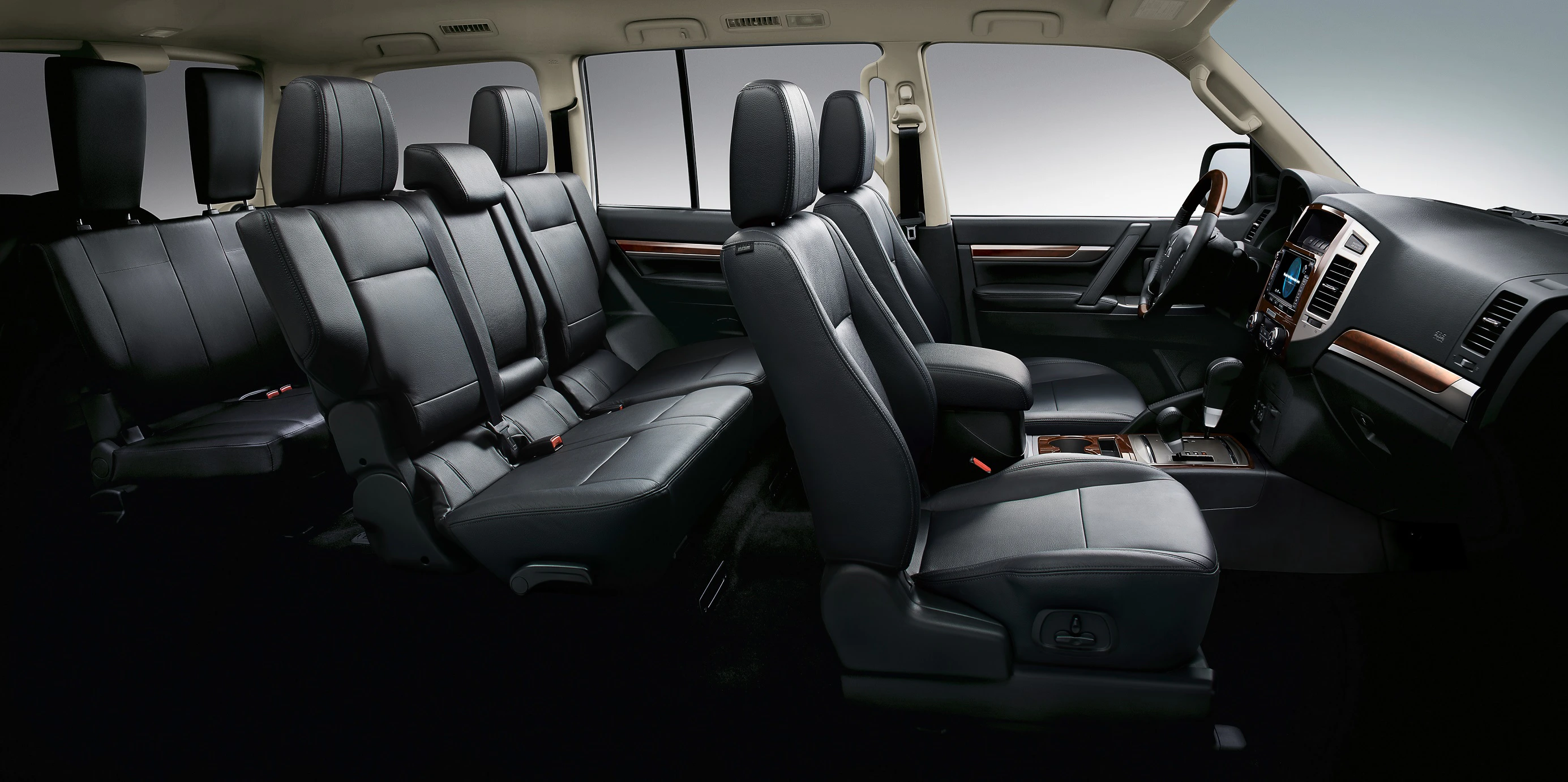 Innenraum eines geräumigen SUVs, sieben schwarze Ledersitze in drei Reihen angeordnet, mit einem modernen Armaturenbrett und Holzverkleidung.