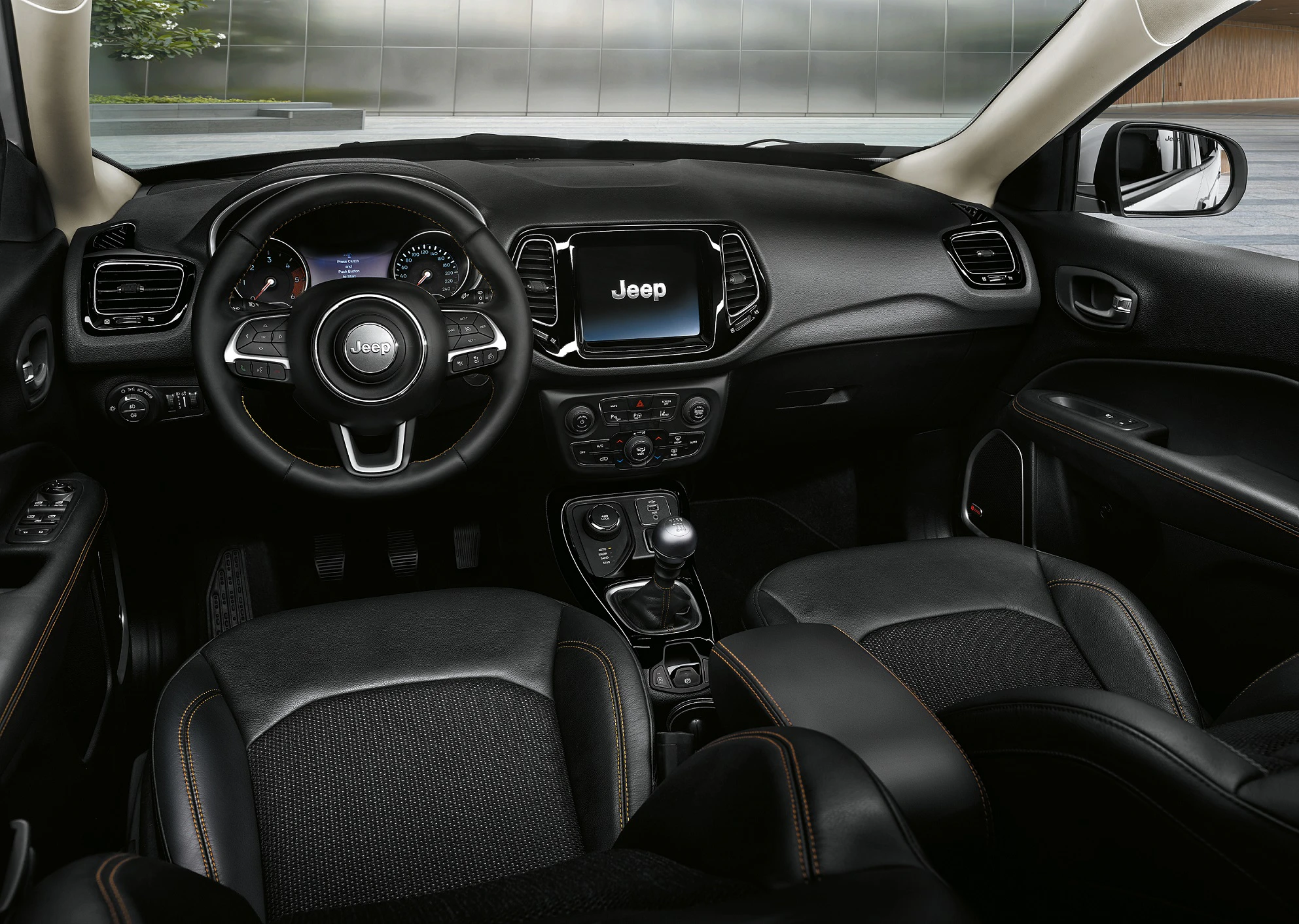 Innenraum eines modernen Jeep SUV mit Lenkrad, Touchscreen-Display und schwarzen Ledersitzen. Das Armaturenbrett zeigt mehrere Bedienelemente.
