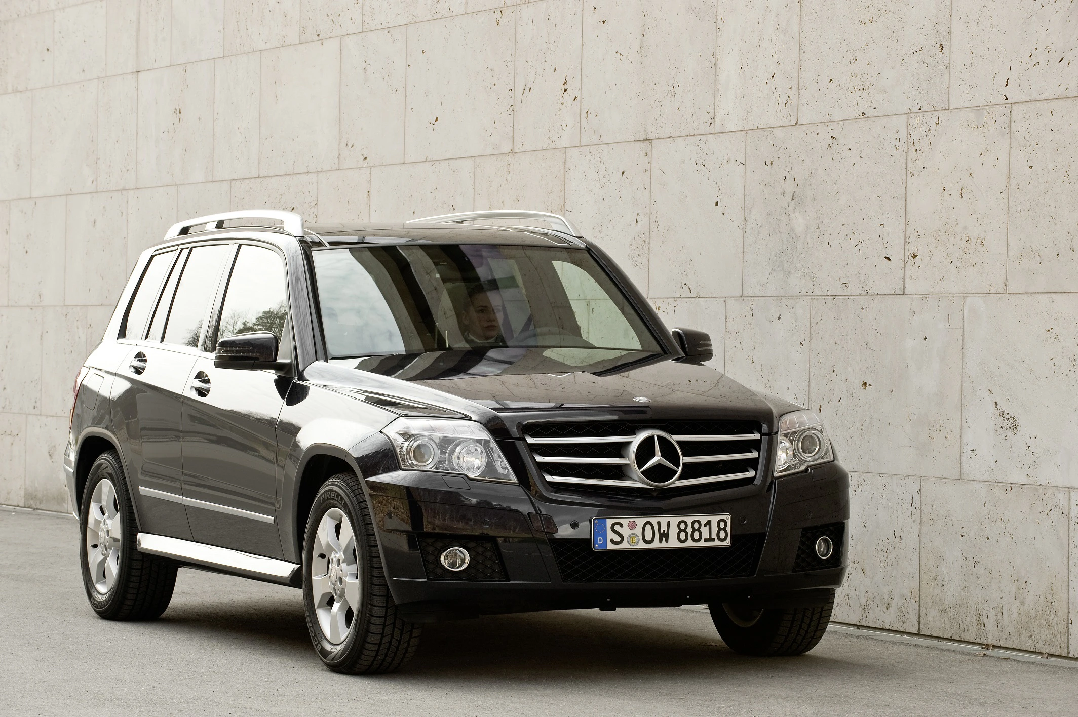 Schwarzer SUV der Marke Mercedes-Benz parkt vor einer Betonwand. Nummernschild sichtbar. Klarer Himmel spiegelt sich auf der Windschutzscheibe.