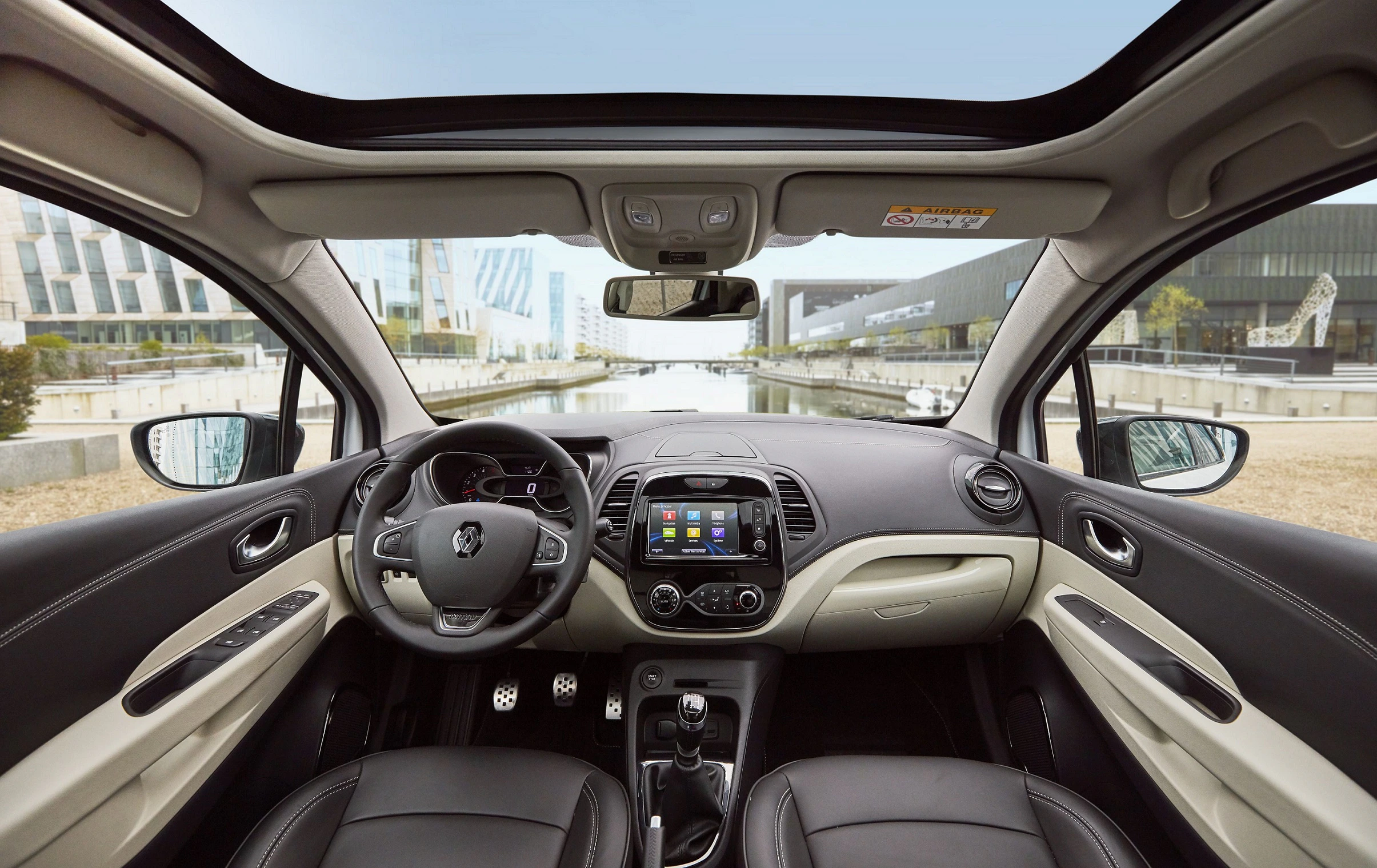 Innenraum eines modernen Autos mit Lederpolstern, Panoramadach und Blick auf städtische Architektur durch die Windschutzscheibe.