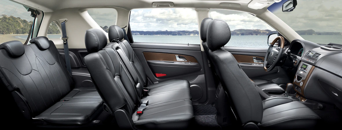 Innenansicht eines Autos mit drei Sitzreihen aus Leder, Blick durch die Fenster auf eine Küstenlandschaft mit Meer und bewölktem Himmel.