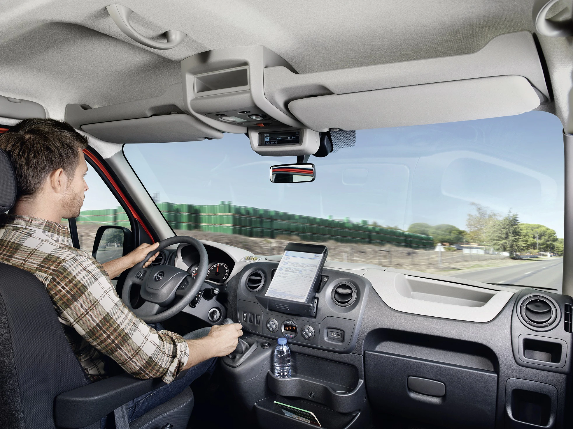 Ein Mann fährt einen Lieferwagen auf einer Straße. Das Interieur ist modern mit einem großen Bildschirm an der Mittelkonsole.