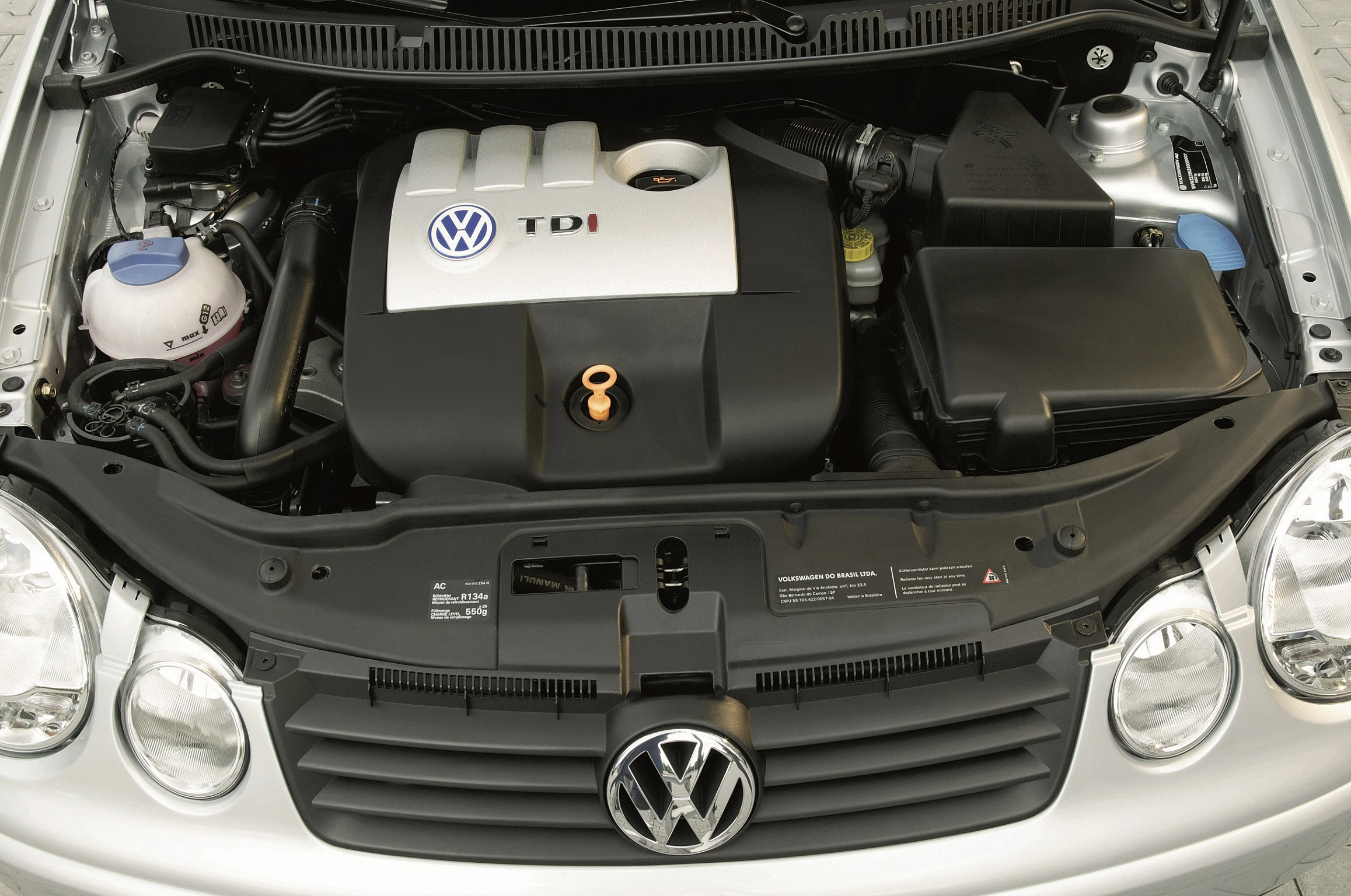 Motorraum eines VW mit TDI-Dieselmotor. Sicht auf Abdeckungen, Kühler und VW-Logo auf dem Kühlergrill.