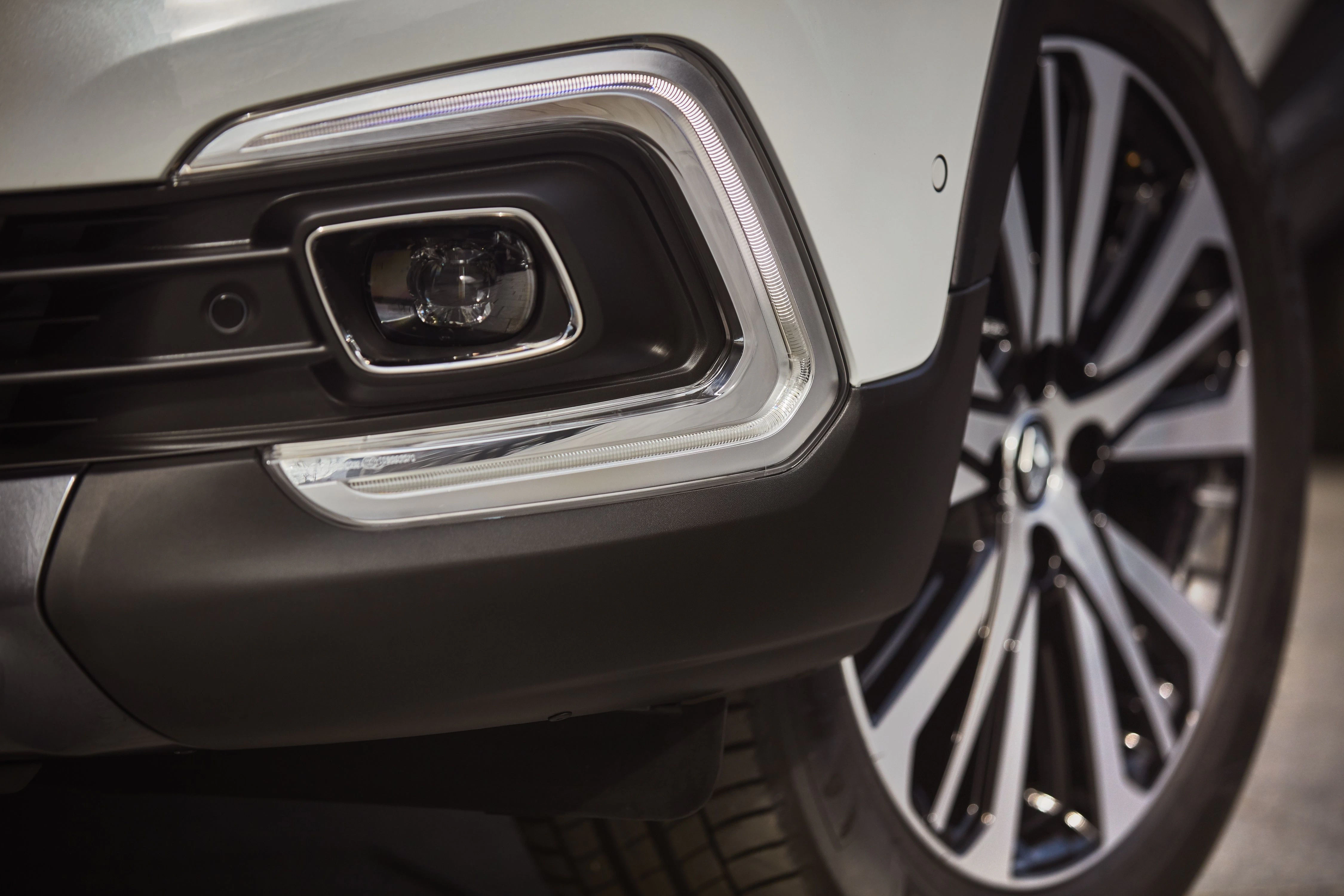 Nahaufnahme eines Autoscheinwerfers und eines stylischen Felgendesigns. Elegantes, modernes Fahrzeugdetail in dunklen Farben.