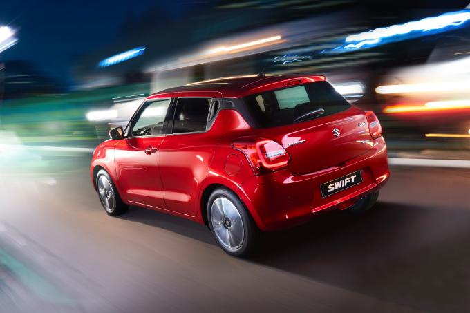 Roter Suzuki Swift fährt mit hoher Geschwindigkeit durch eine beleuchtete Stadt in der Nacht, unscharfer Hintergrund.