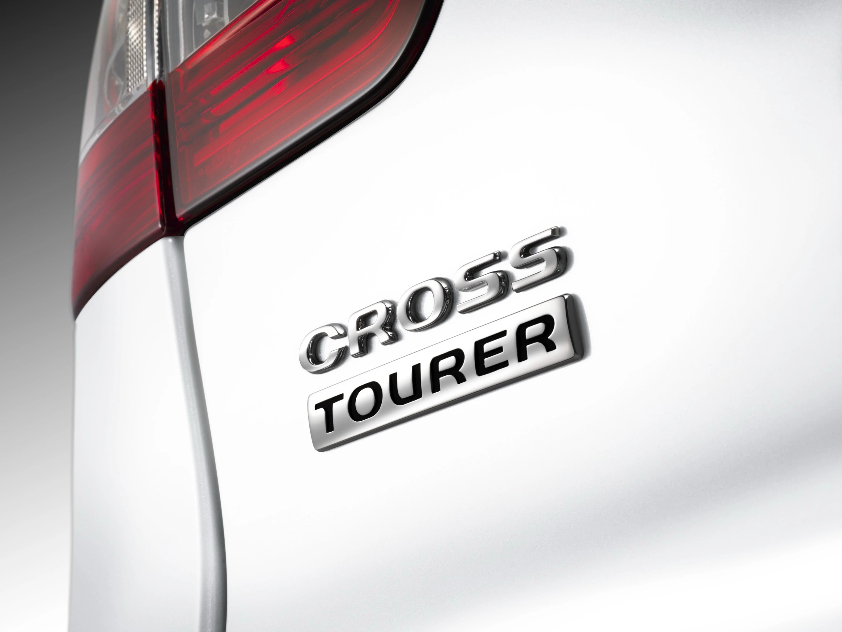 Nahaufnahme des Heckbereichs eines Fahrzeugs mit der Aufschrift "Cross Tourer" in glänzenden Buchstaben auf weißem Lack.